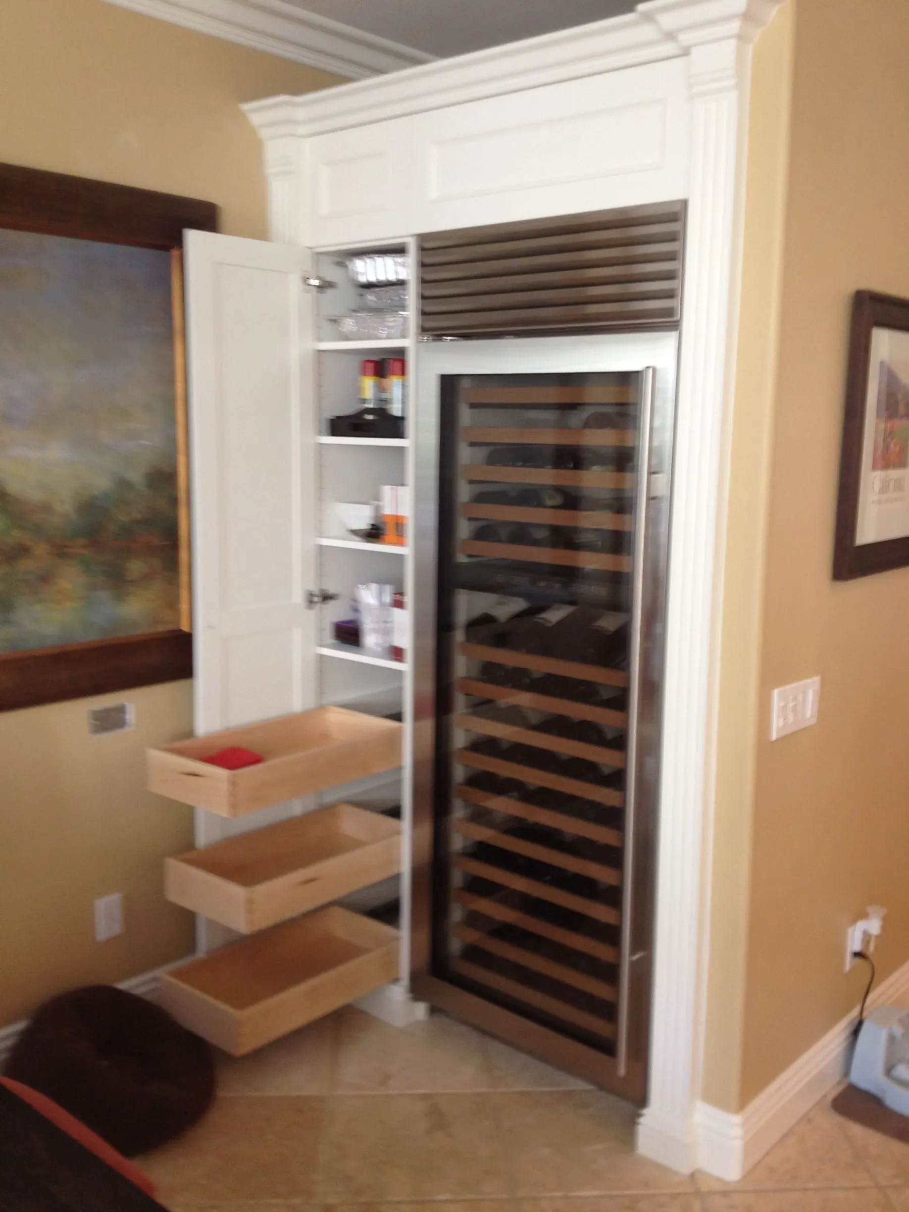 Kitchen pantry cabinet with open door, pull-out drawers, and a wine rack in a beige room.