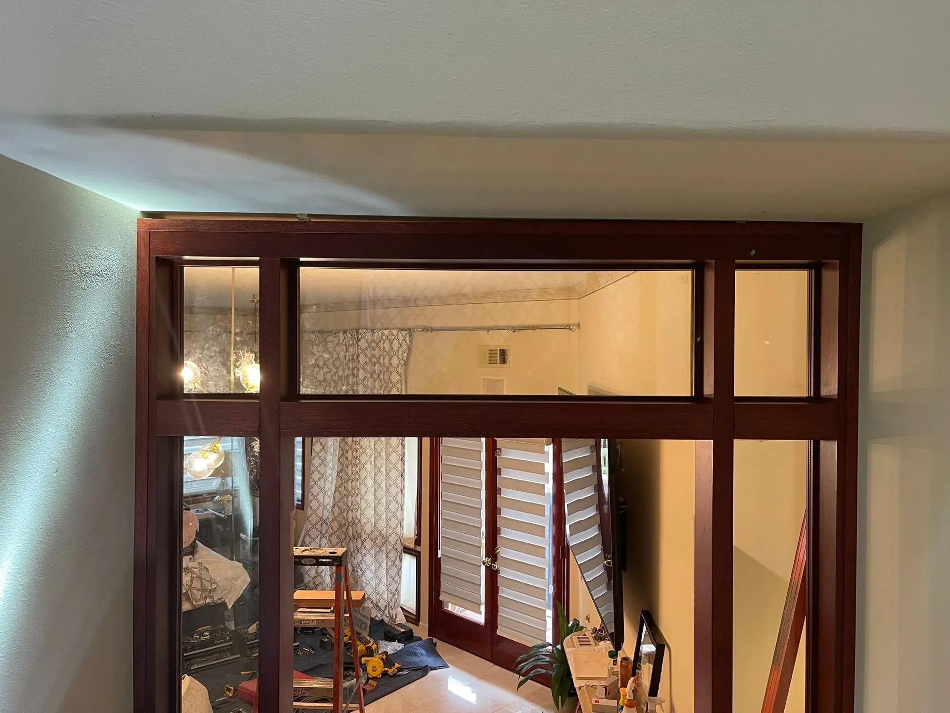 Indoor hallway with a wooden-framed opening into a room, showing a bed and windows with blinds.