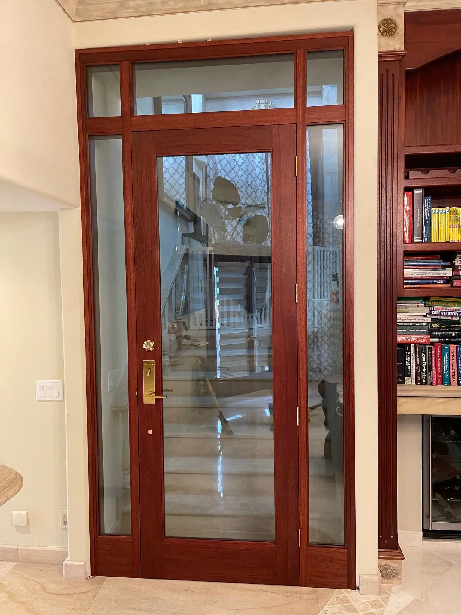 Wood-framed glass door with sidelights and transom in a living room, with a bookshelf to the right.