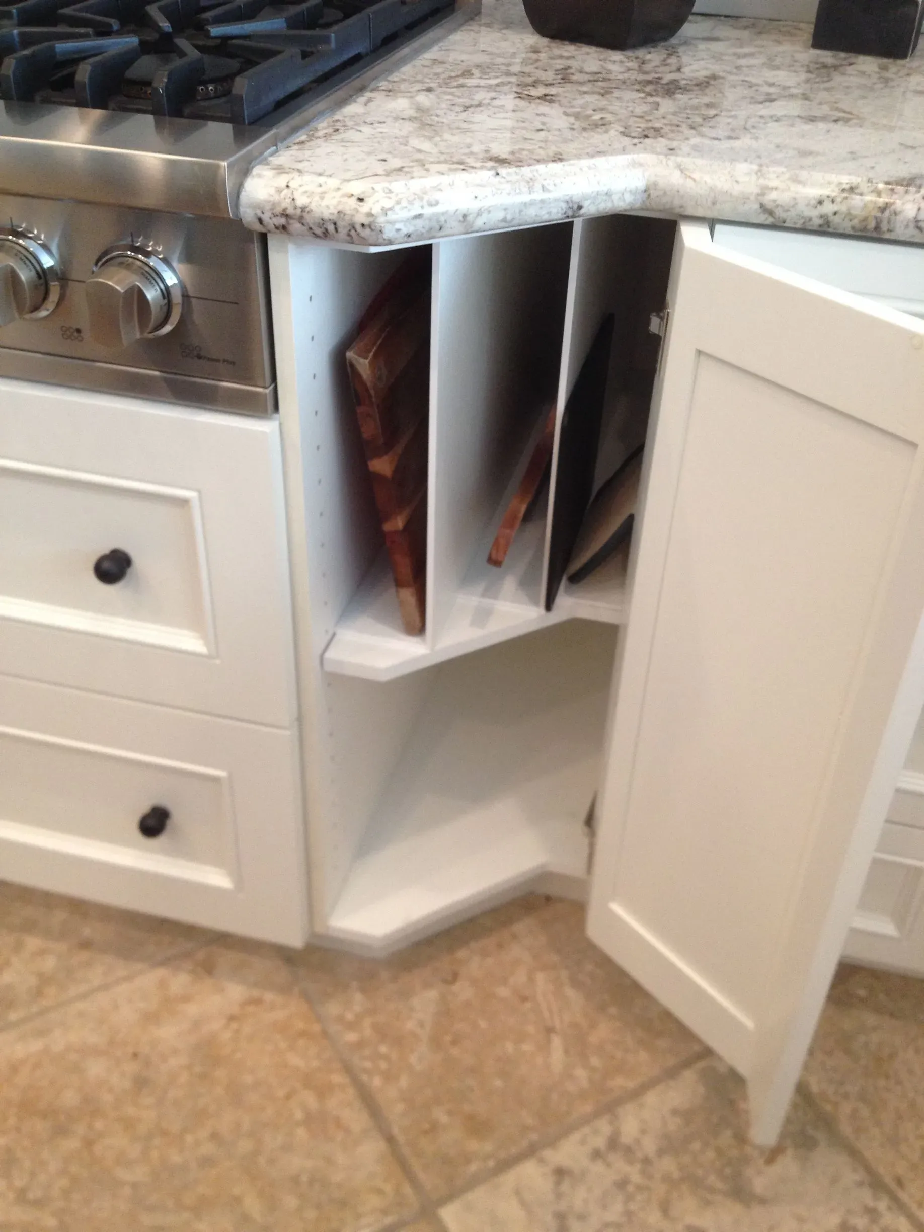 Open kitchen cabinet with pull-out corner shelves under a countertop, beside a stove.