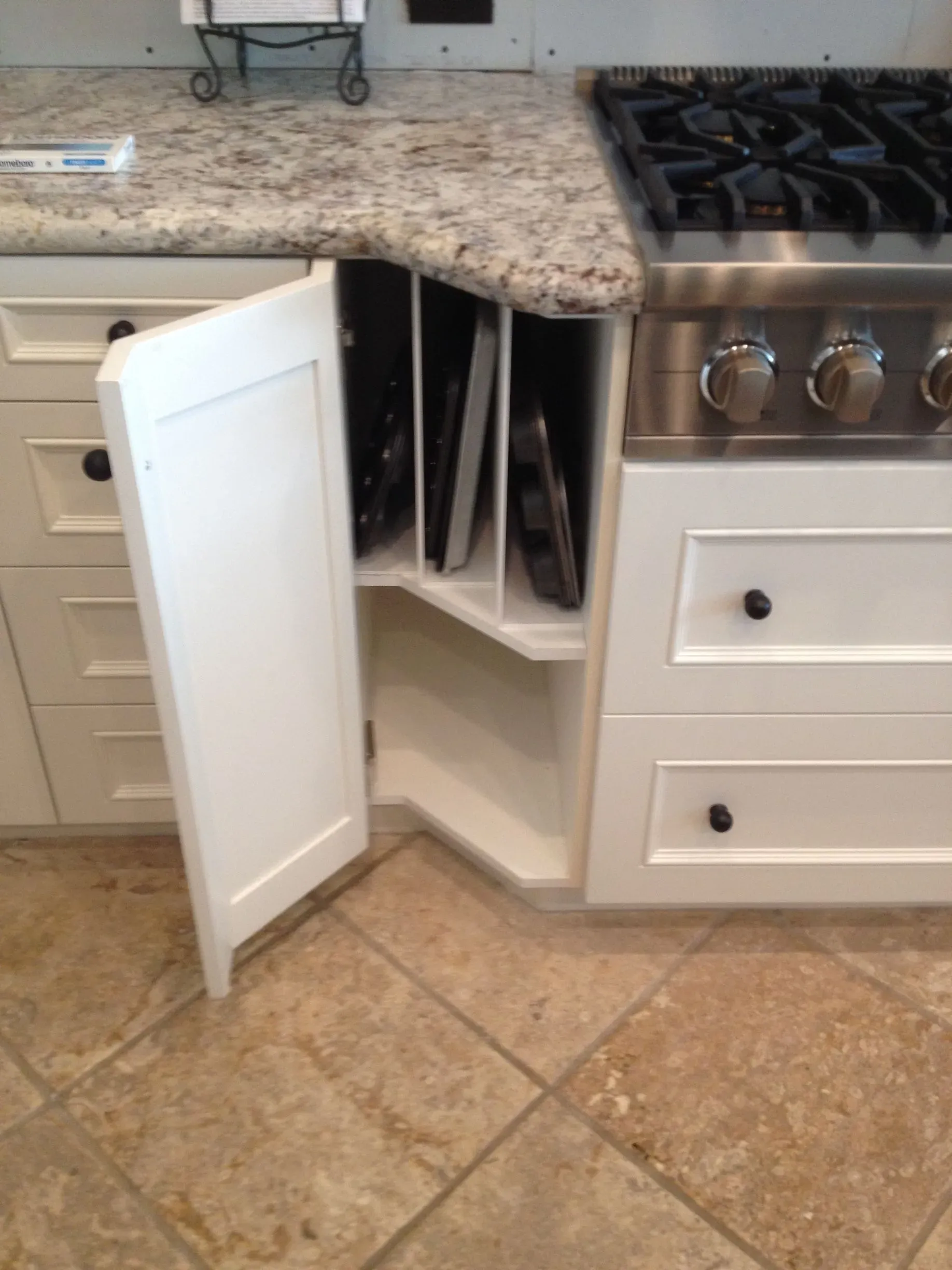 Corner kitchen cabinet with a white door open, showing shelves beside a stove and granite countertop.