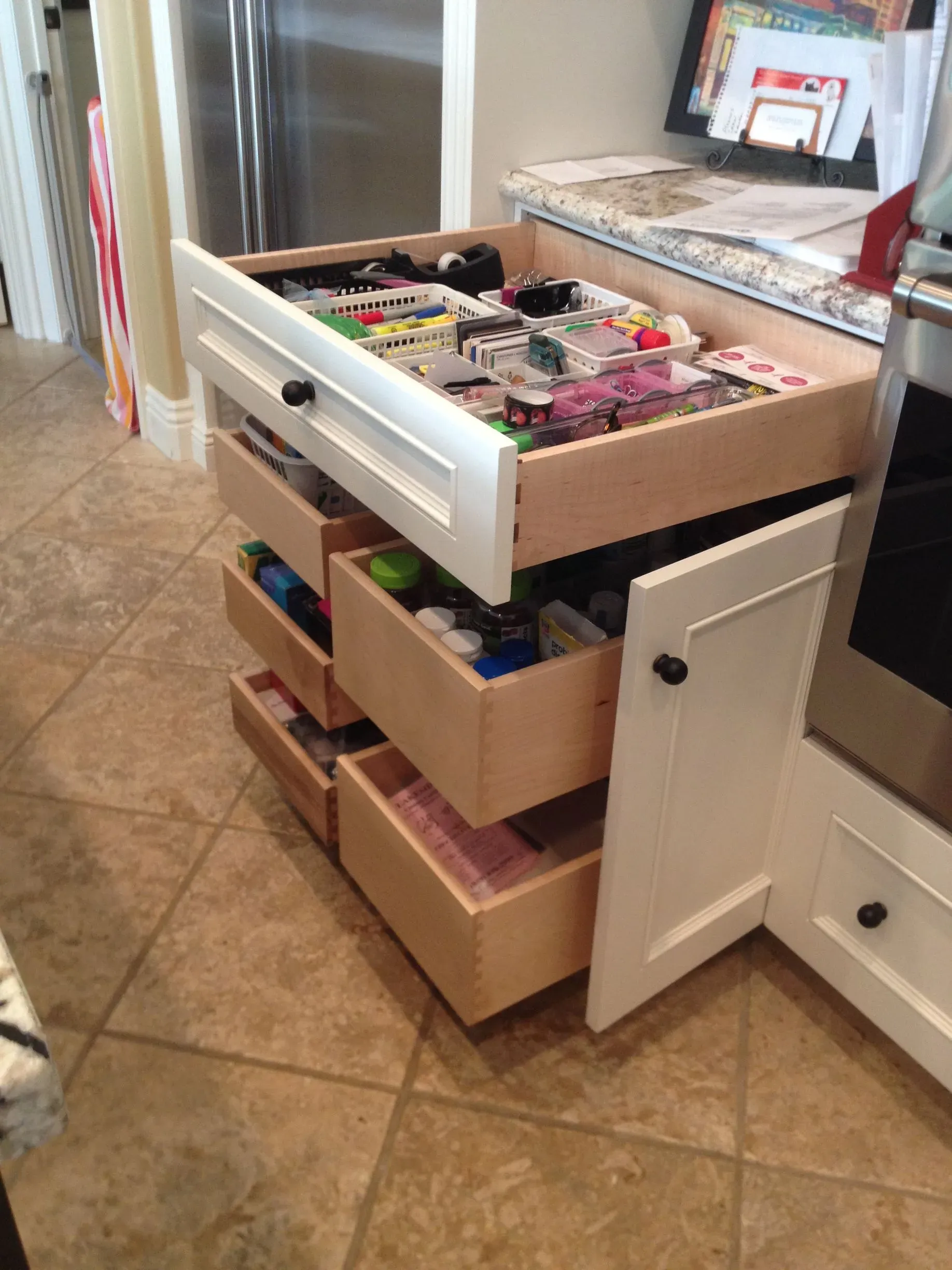 Kitchen drawer organizer with boxes of craft supplies and a drawer pulled open on a tiled floor