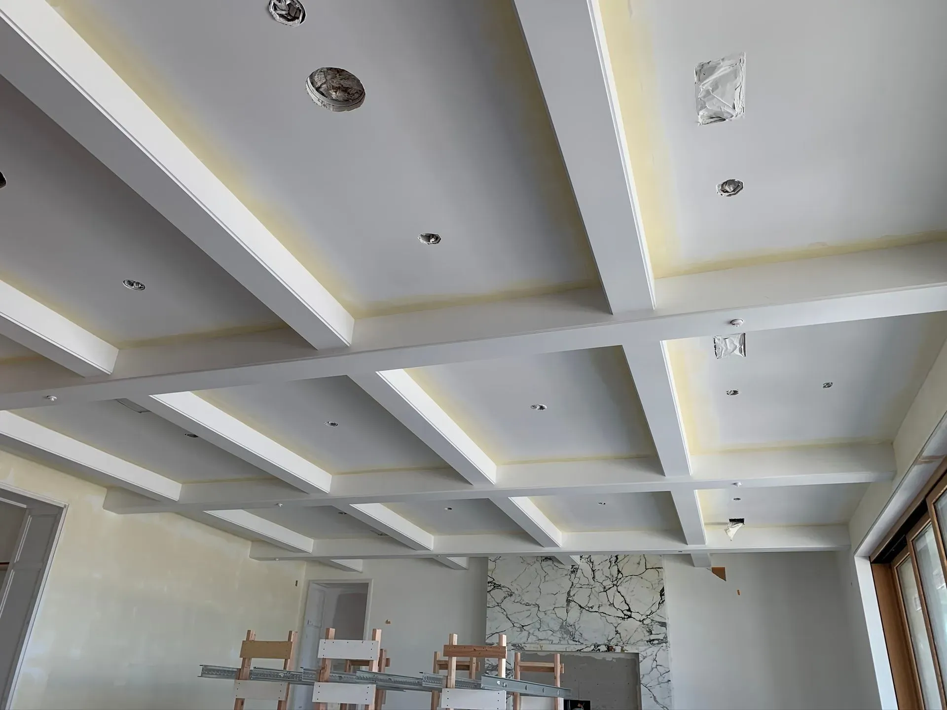 Modern room with white coffered ceiling, recessed lights, and large windows along the right side