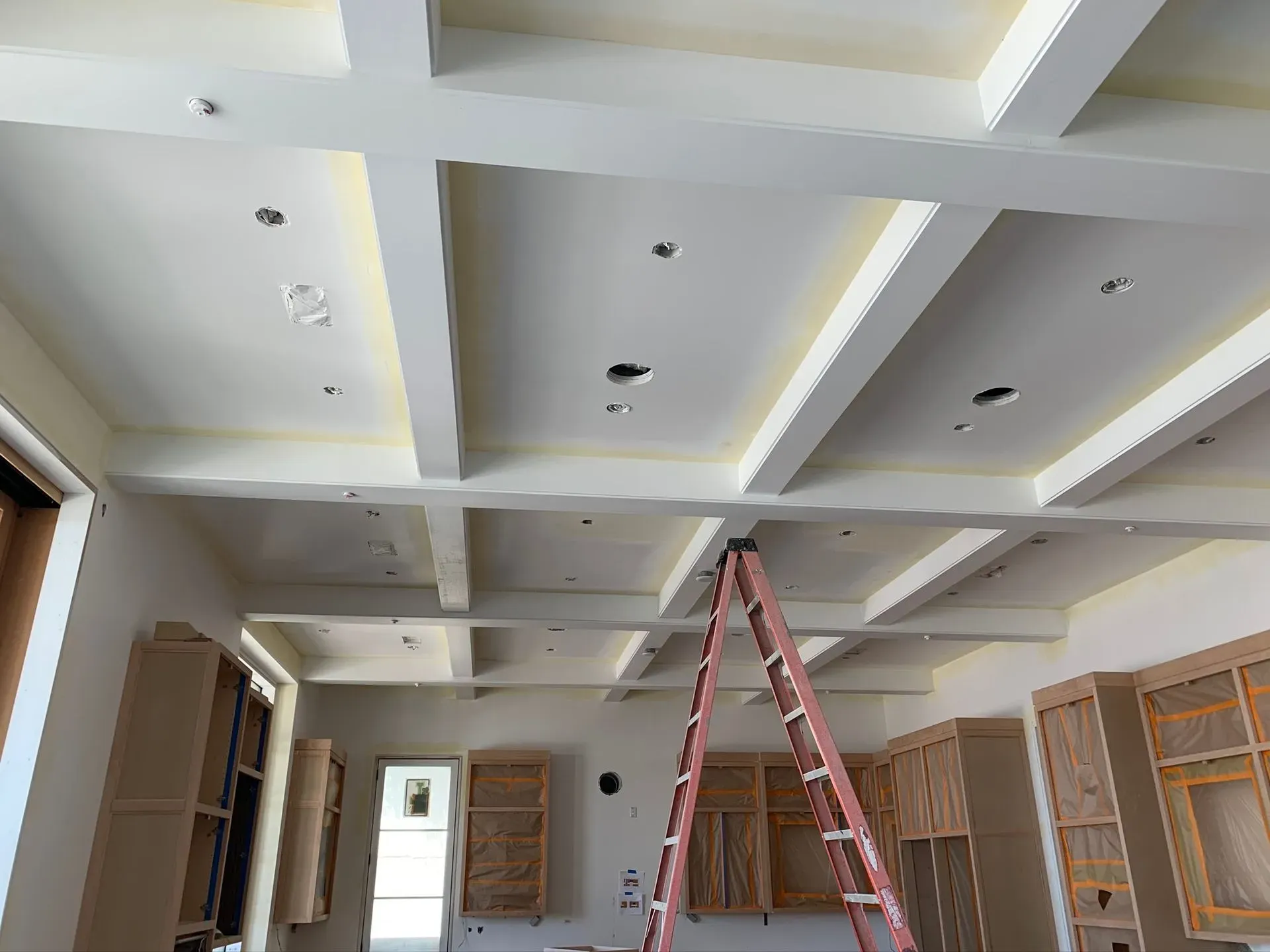 Interior room under construction with a red ladder under a coffered white ceiling and open shelving.