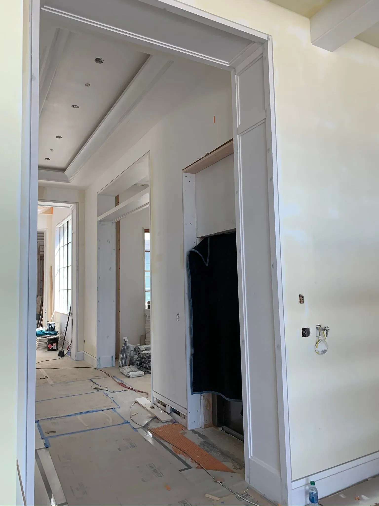 Hallway under renovation with white walls, exposed floor coverings, and construction debris.