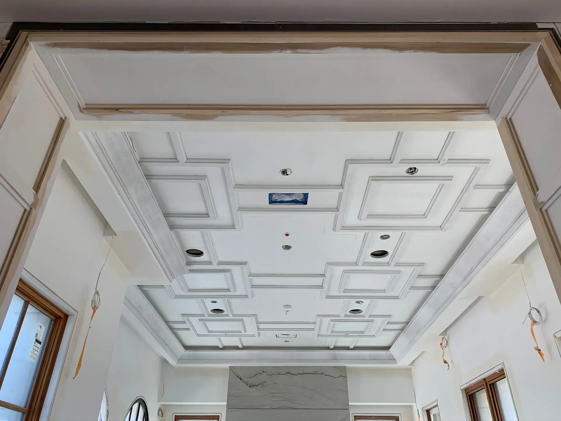 White ornate ceiling with recessed square panels and light fixtures in a hallway