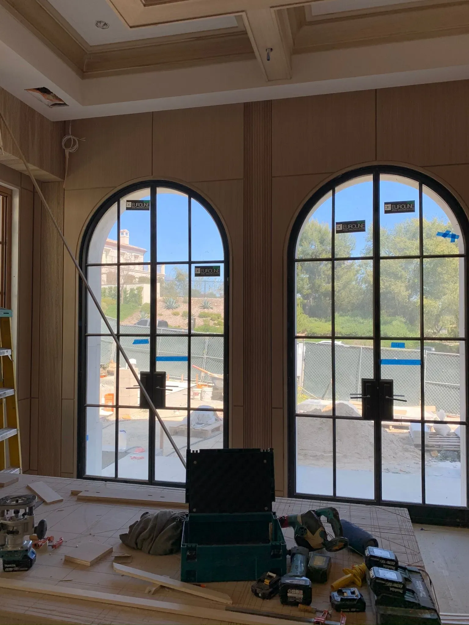 Interior under renovation with arched windows, scattered tools, and construction materials on the floor