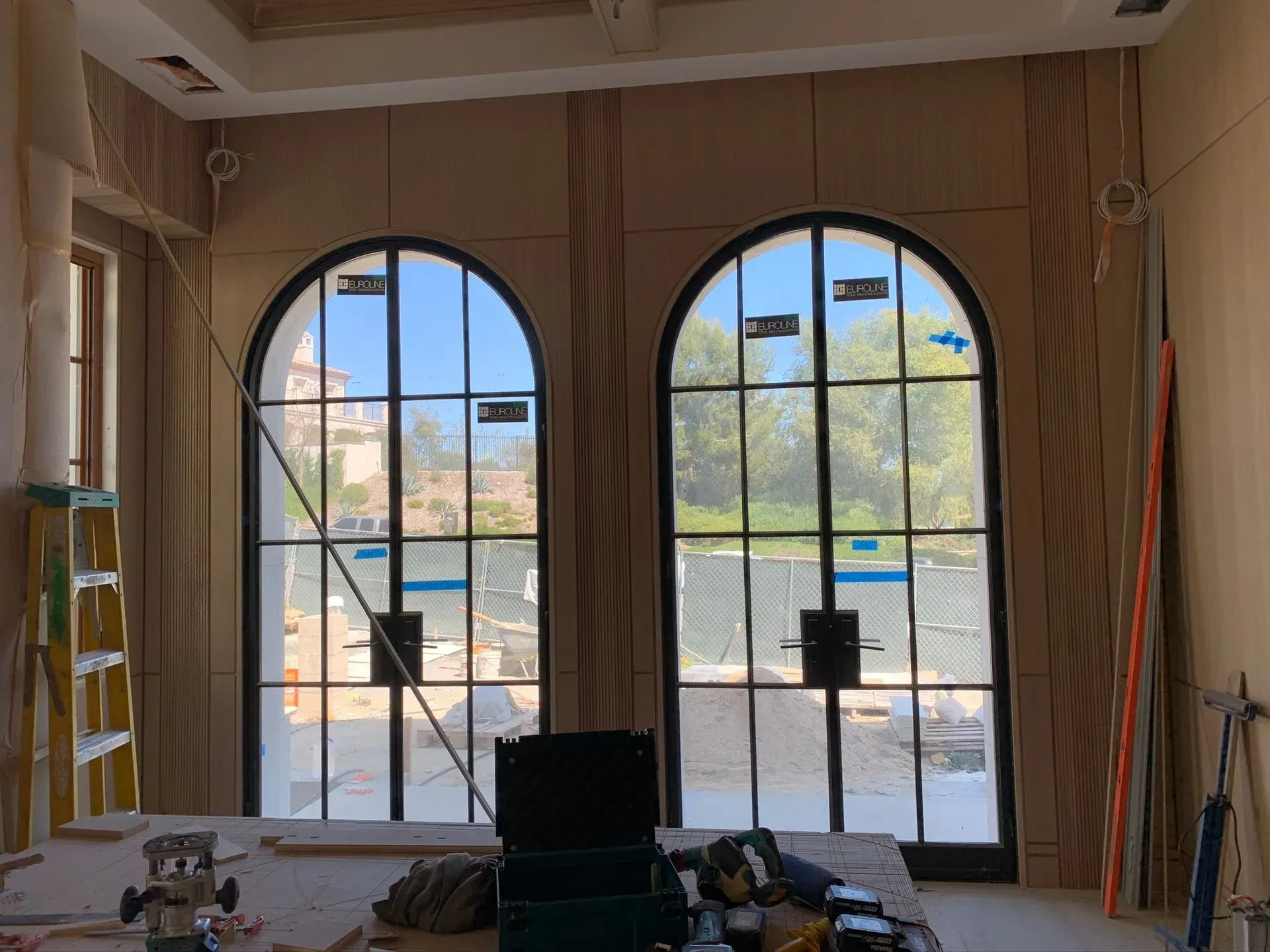 Empty room with two large arched windows, sunlight, and construction materials on the floor