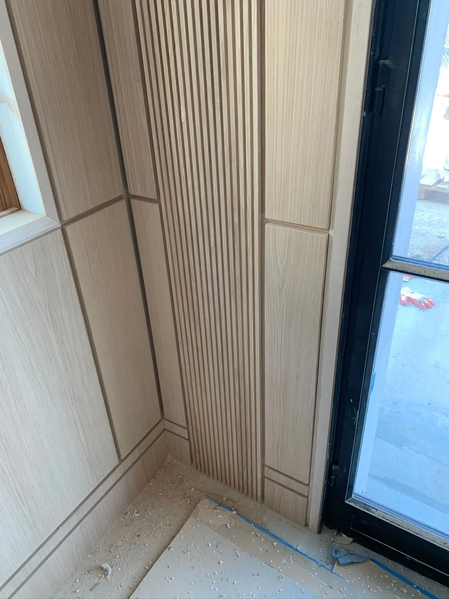 Wood-paneled wall corner beside a glass door, with a bright striped light reflection on the paneling.