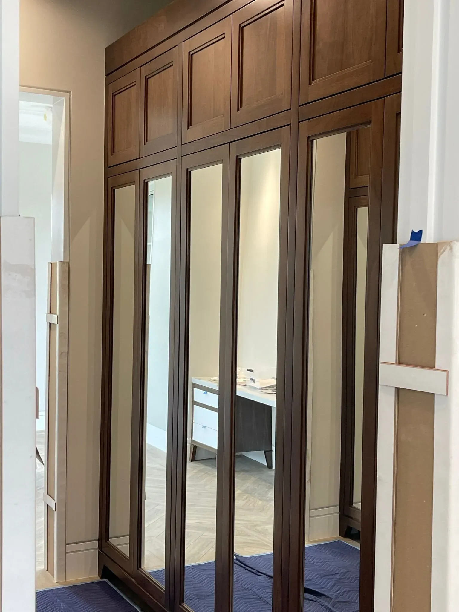 Built-in mirrored closet doors beneath wood-paneled cabinets in a hallway