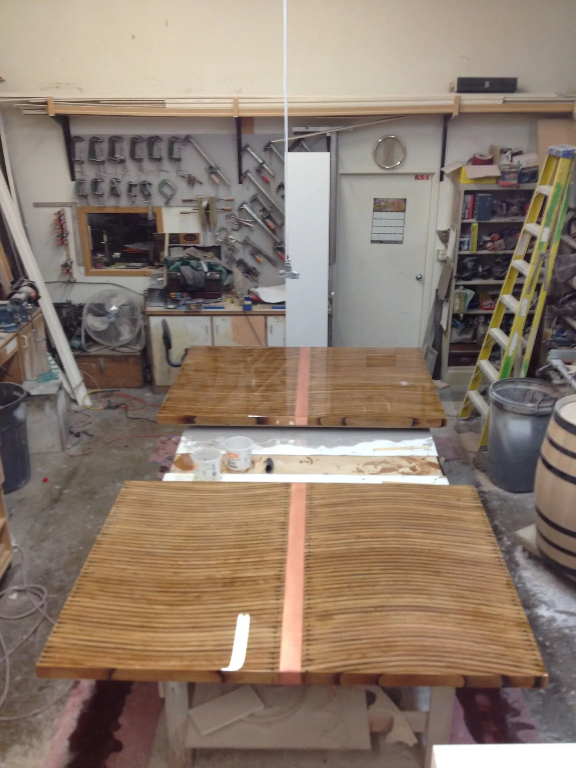 Workshop with two wooden tables, a long wooden strip, and a yellow ladder in the background.