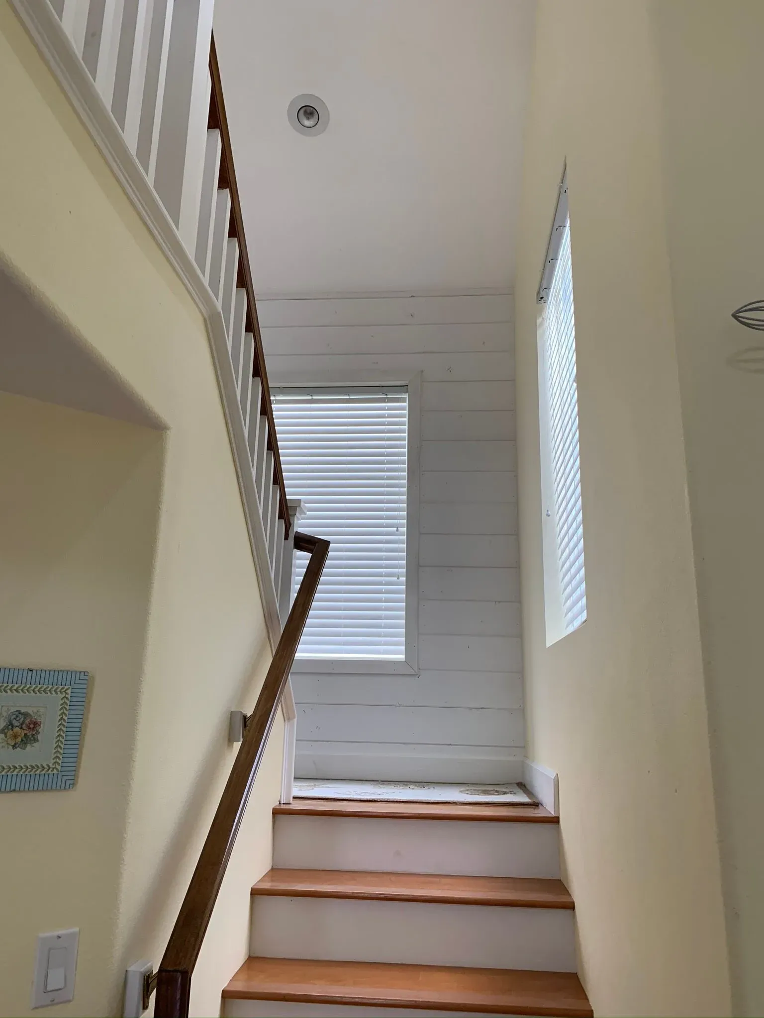 Staircase with white walls, wooden steps, and a windowed landing in a narrow entryway