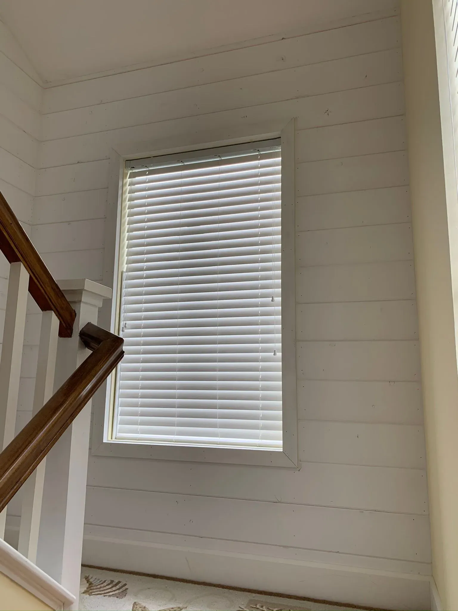Staircase wall with a small window and white blinds in a bright interior.
