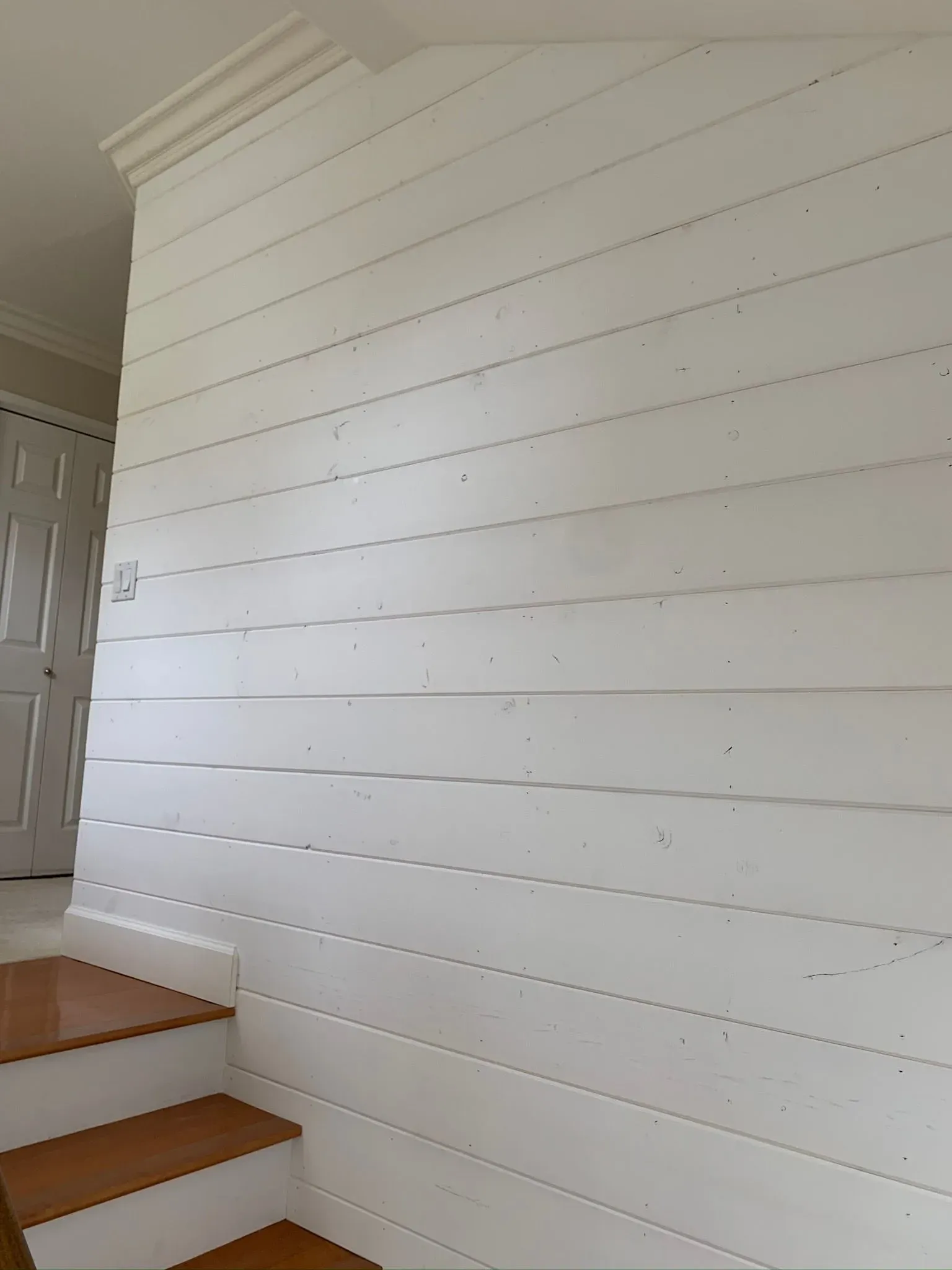 White shiplap wall beside wooden stairs and a doorway in a home interior