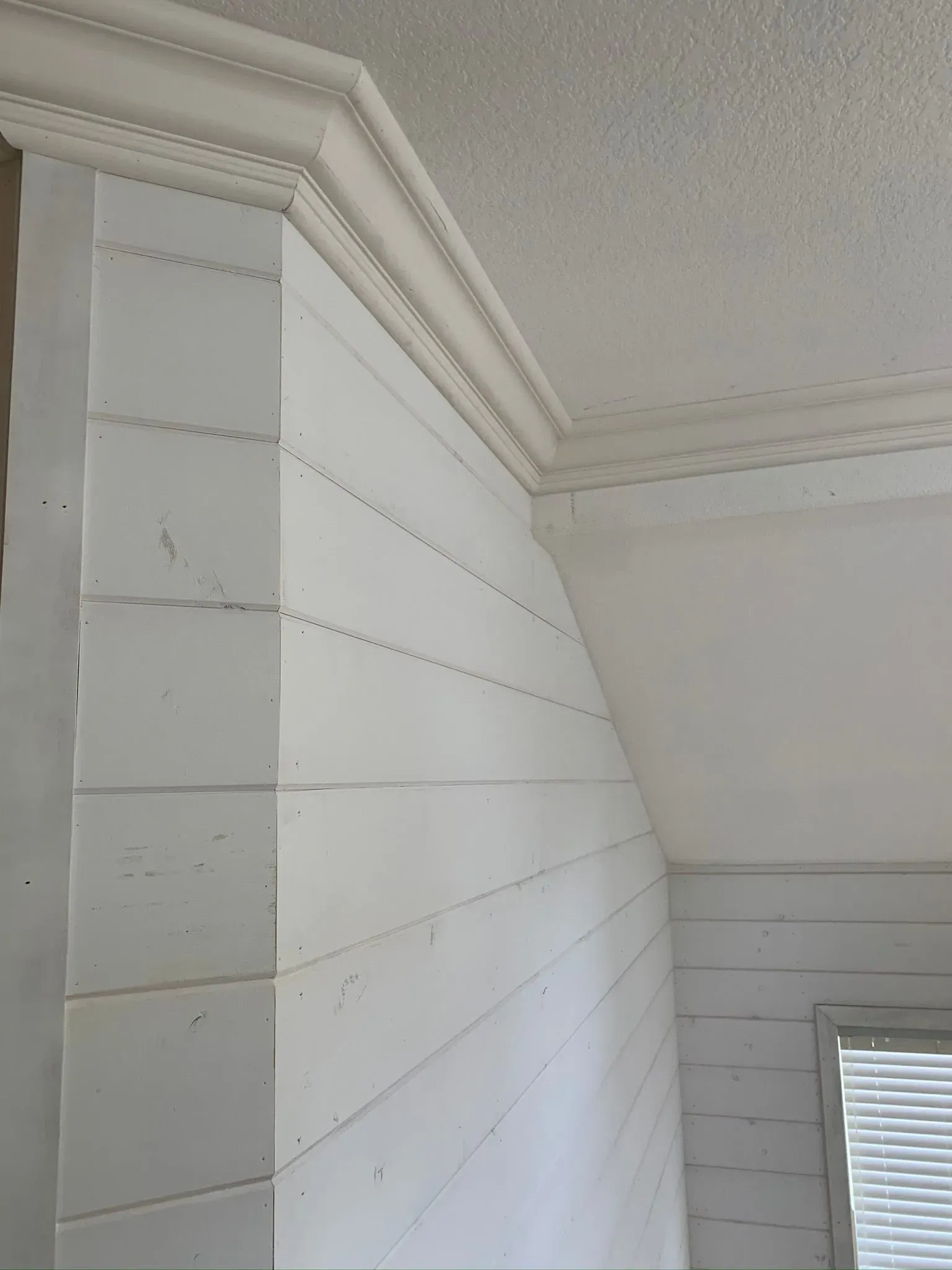 White paneled wall corner with decorative crown molding and a small window below