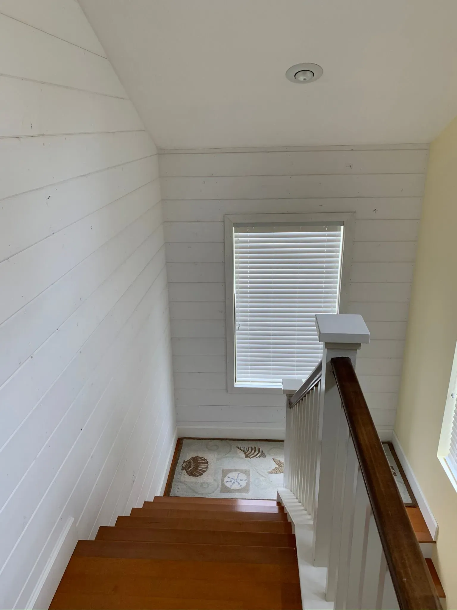 Staircase descending to a landing with a window and white walls, viewed from the top.