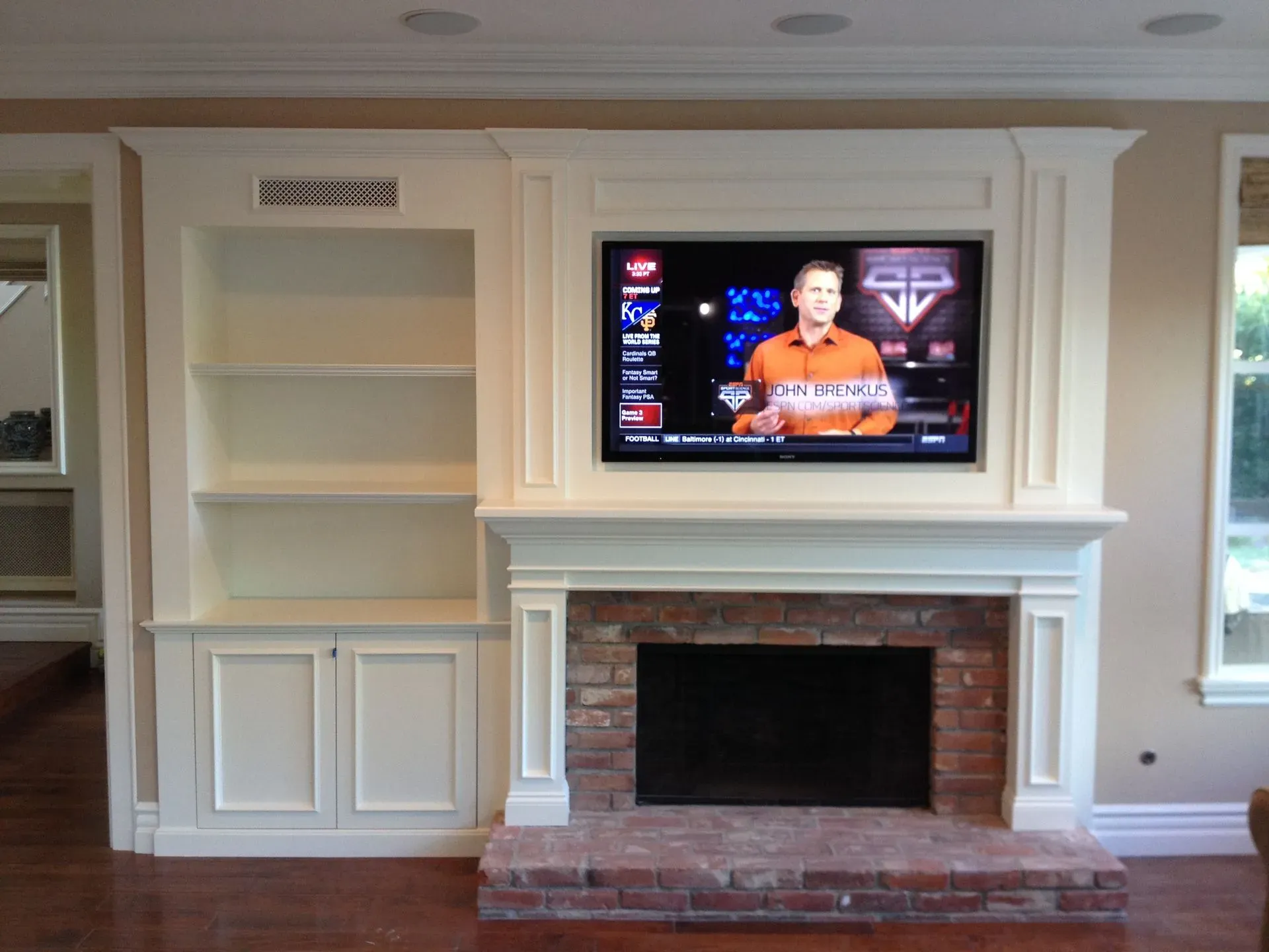 Built-in white cabinetry with a brick fireplace and wall-mounted TV in a living room.