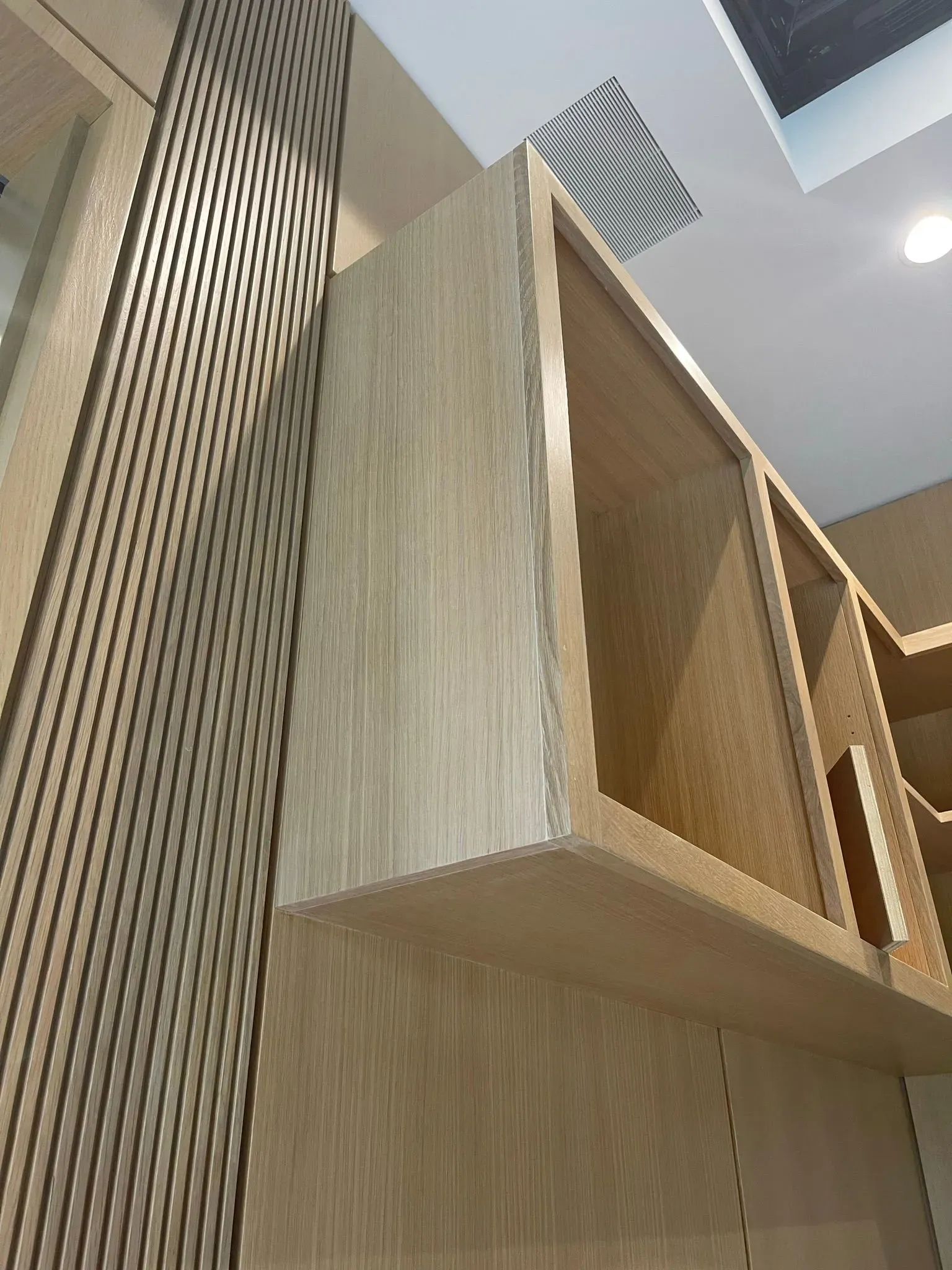Wooden wall-mounted shelf in a modern interior with vertical slat paneling and ceiling vents above