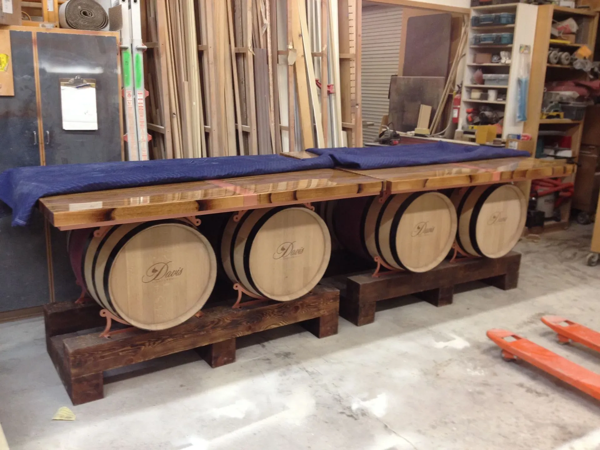 Wooden wine barrels beneath a blue-cushioned tasting table in a workshop-like room