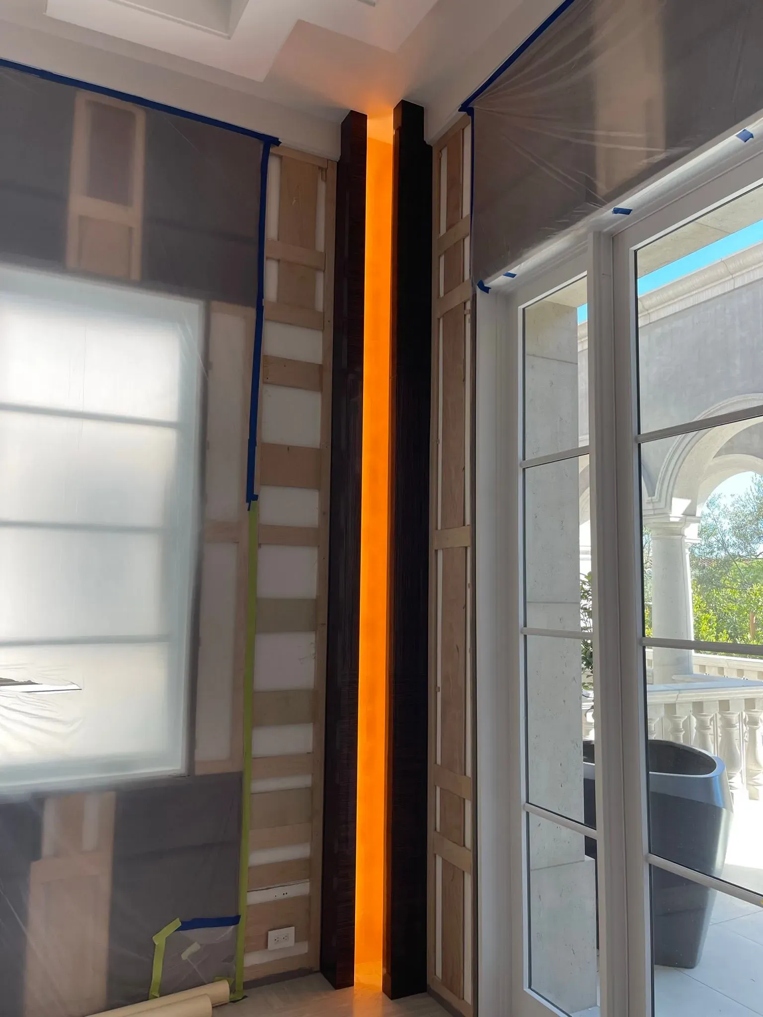 Interior corner with a glowing orange vertical light strip beside blinds and a glass door.