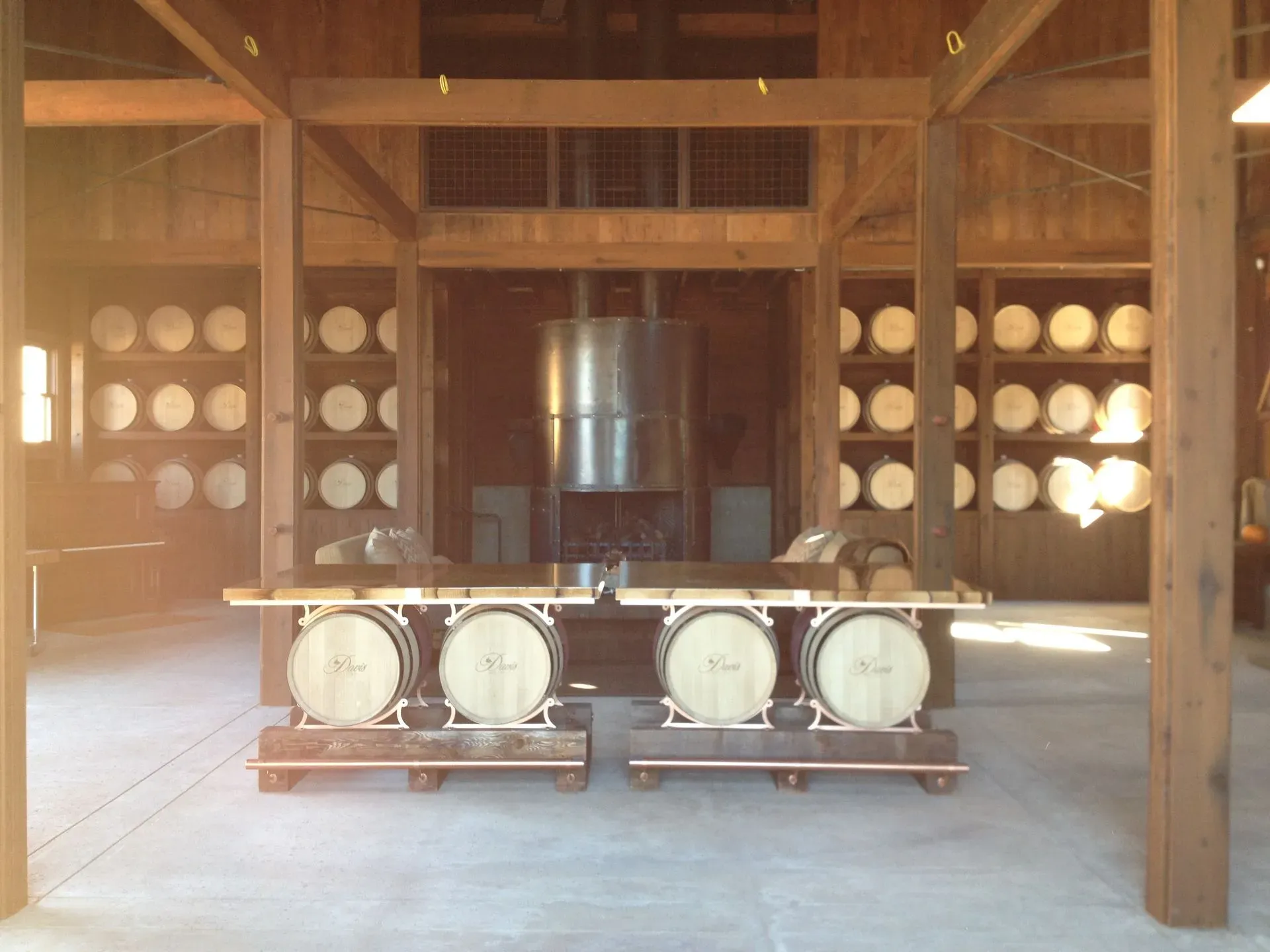 Wooden barrel-aging room with stacked casks and two metal racks of white barrels in the foreground