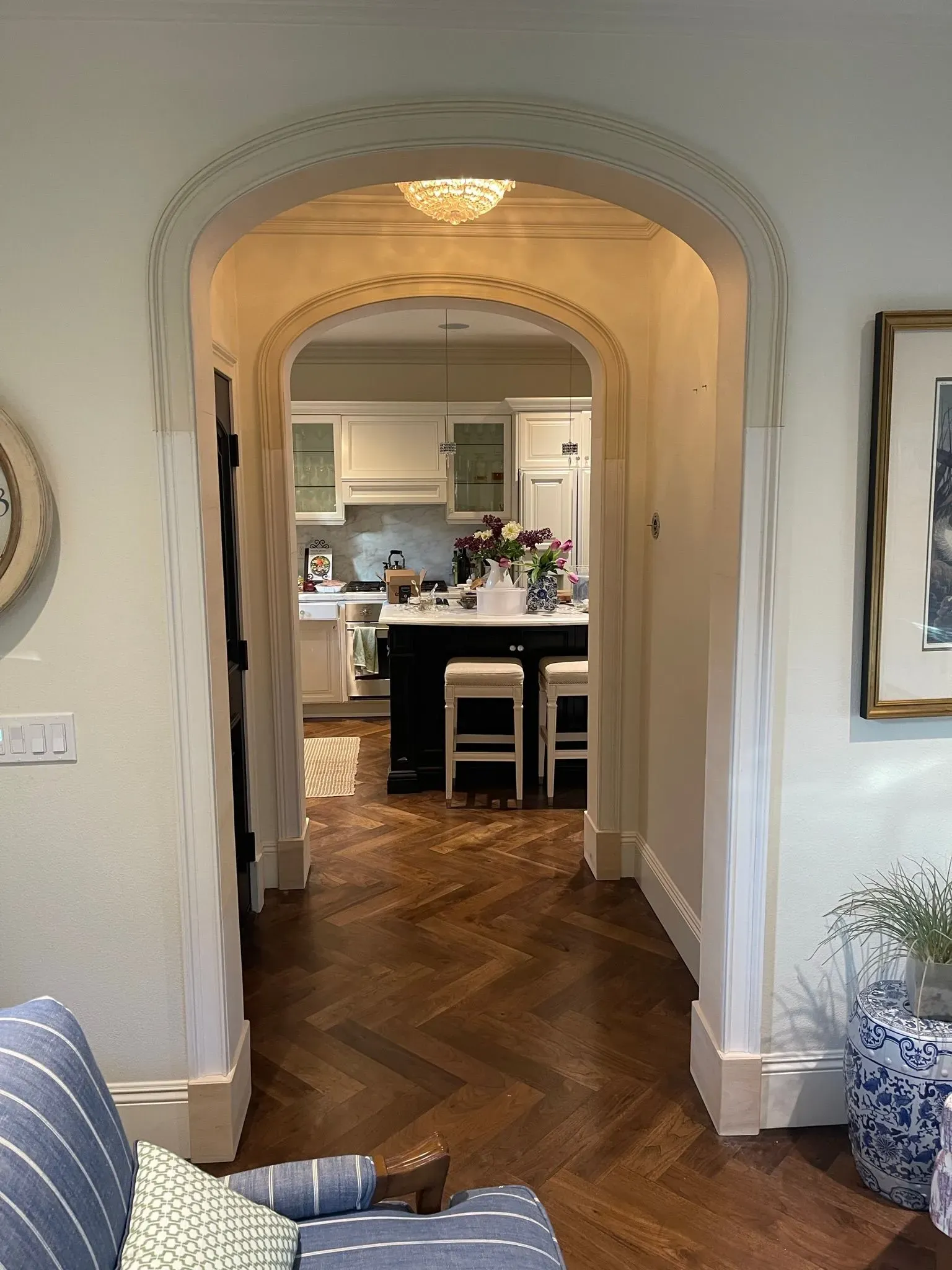 Arched hallway opening to a bright kitchen with dark wood floors and a central island with stools and flowers