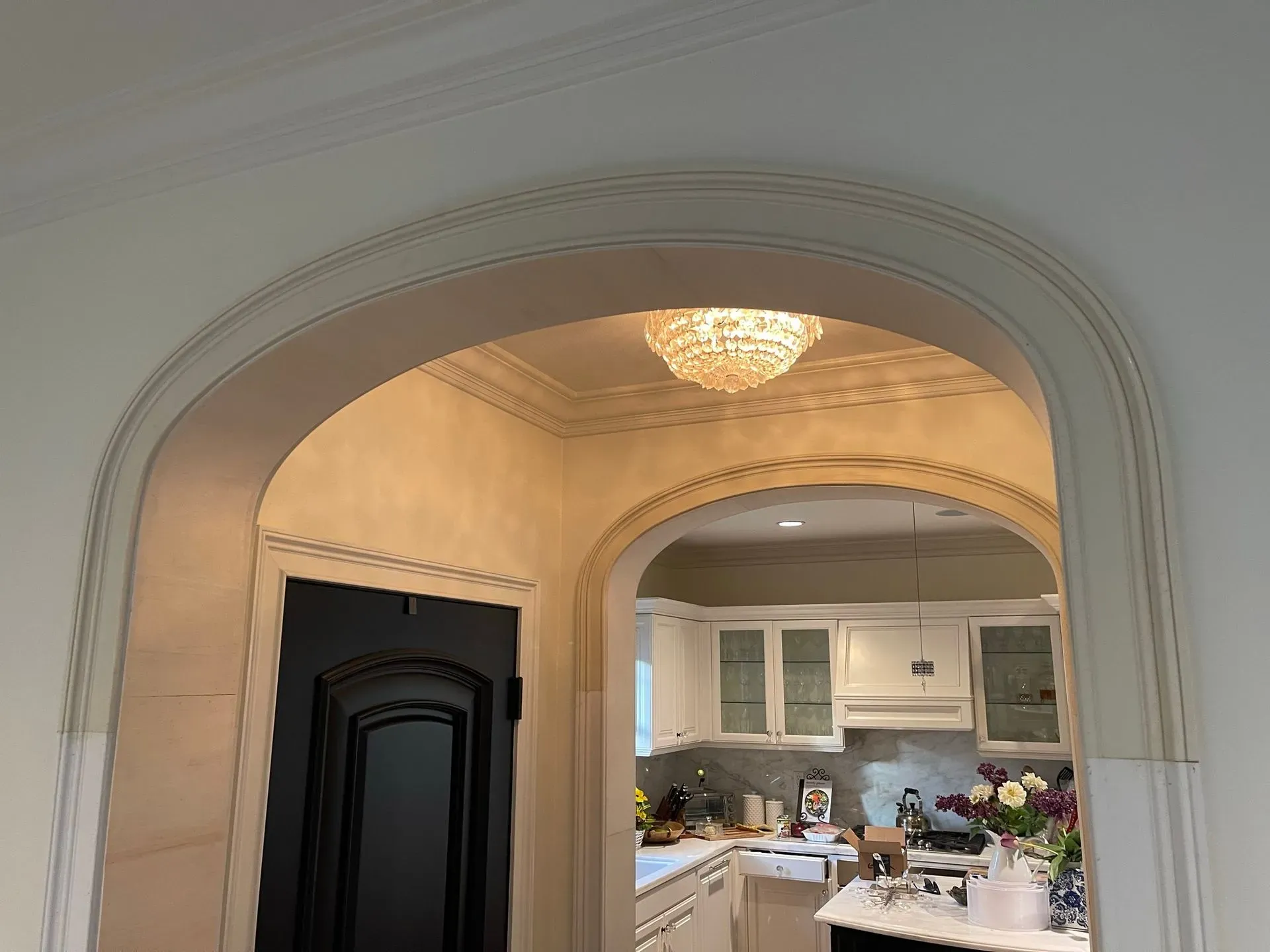 Arched doorway to a bright kitchen with white cabinets and a chandelier, seen from a hall