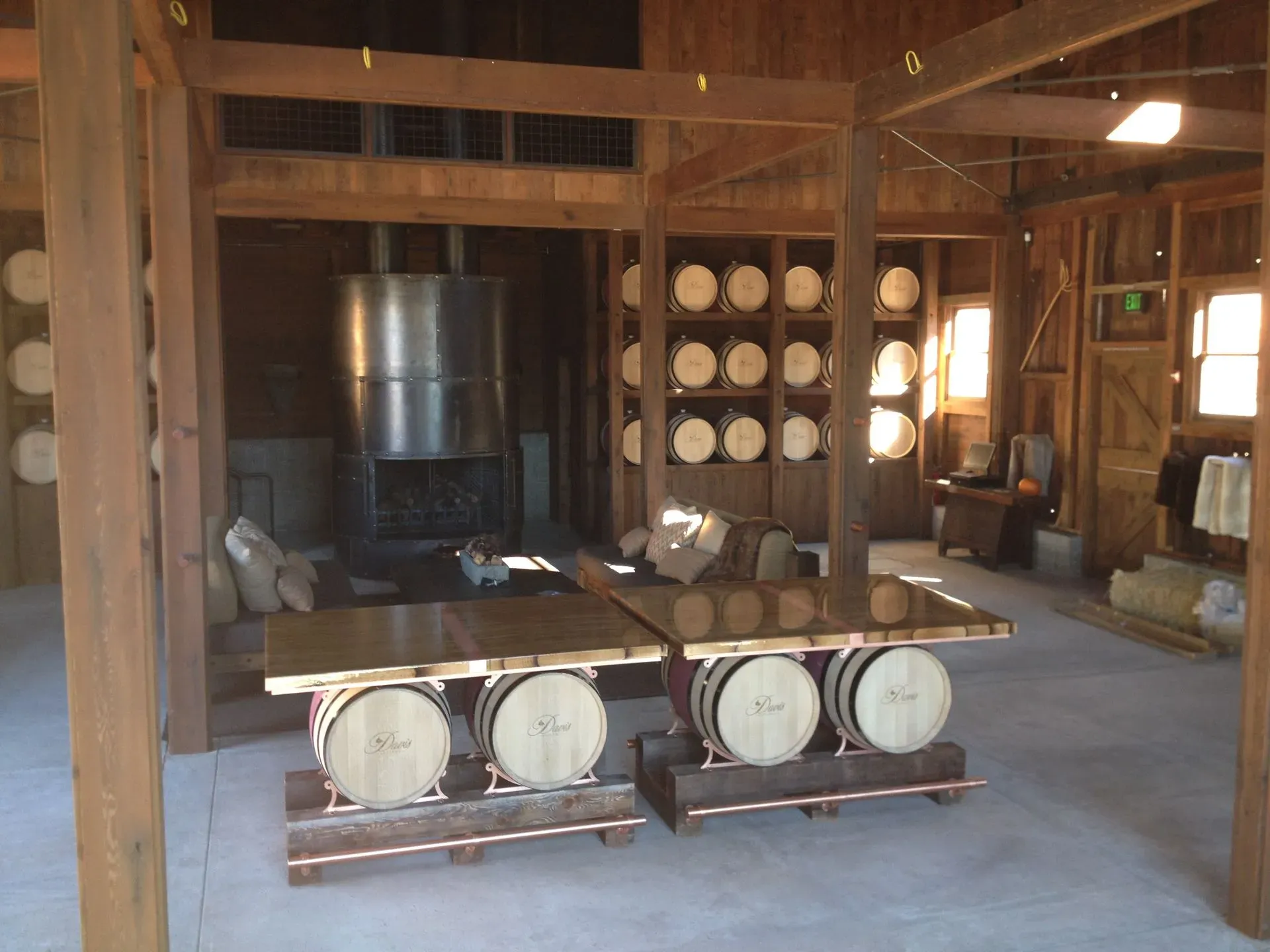 Rustic room with wooden beams, a large metal stove, and barrels lining the back wall.
