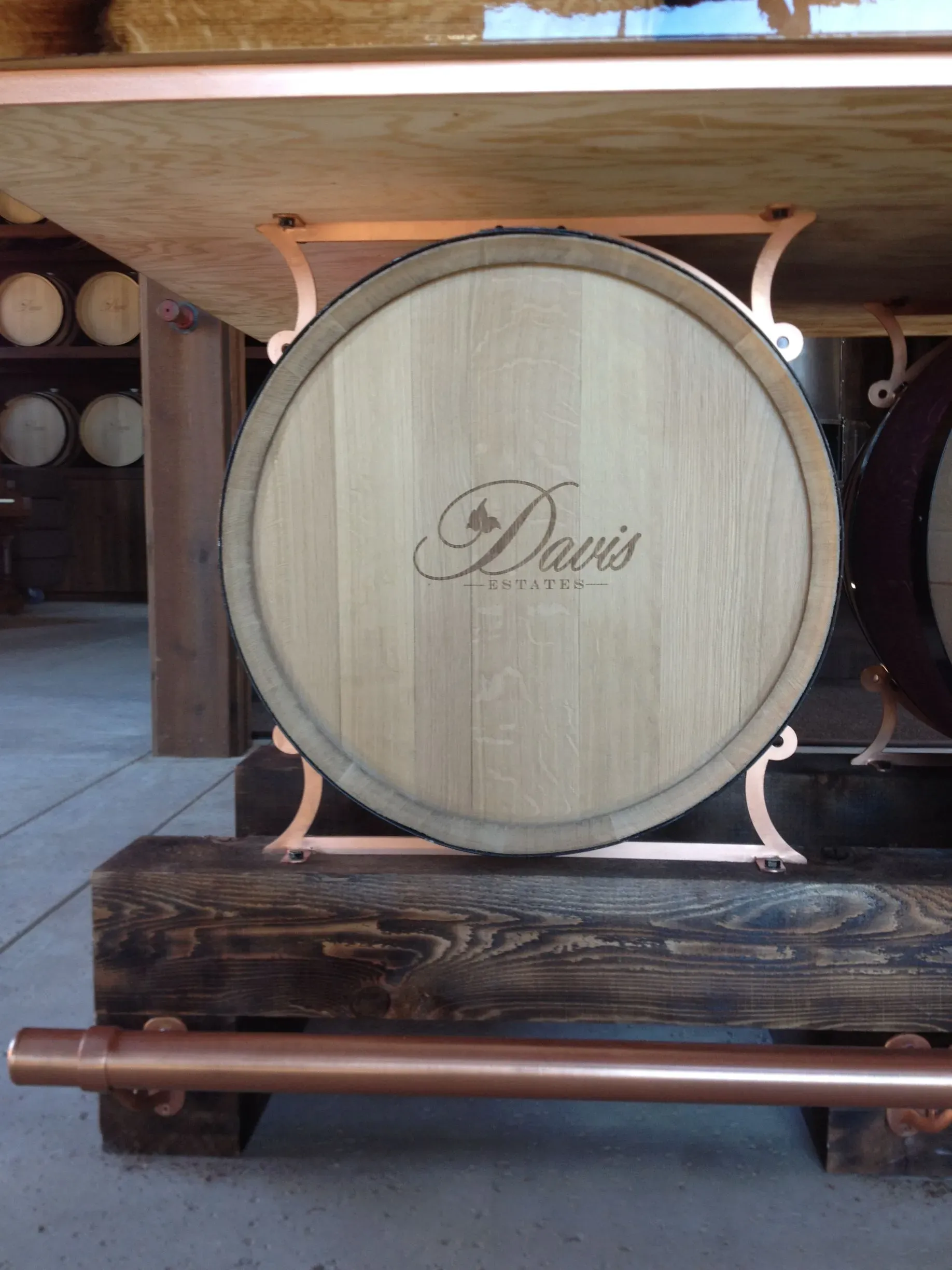 Large wooden wine barrel labeled “Davis” in a cellar, with stacked barrels in the background.