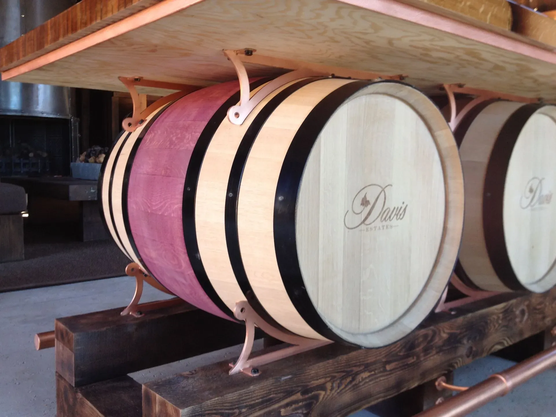 Wooden barrels stacked on a rack in a cellar, including a pink and black barrel end.