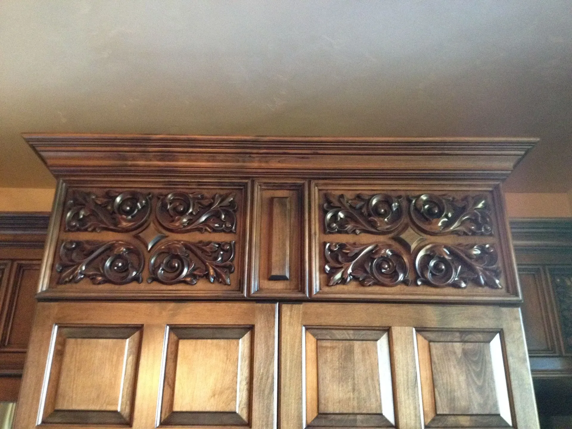 Ornate dark wooden cabinet top with carved lattice panels and crown molding against a wall