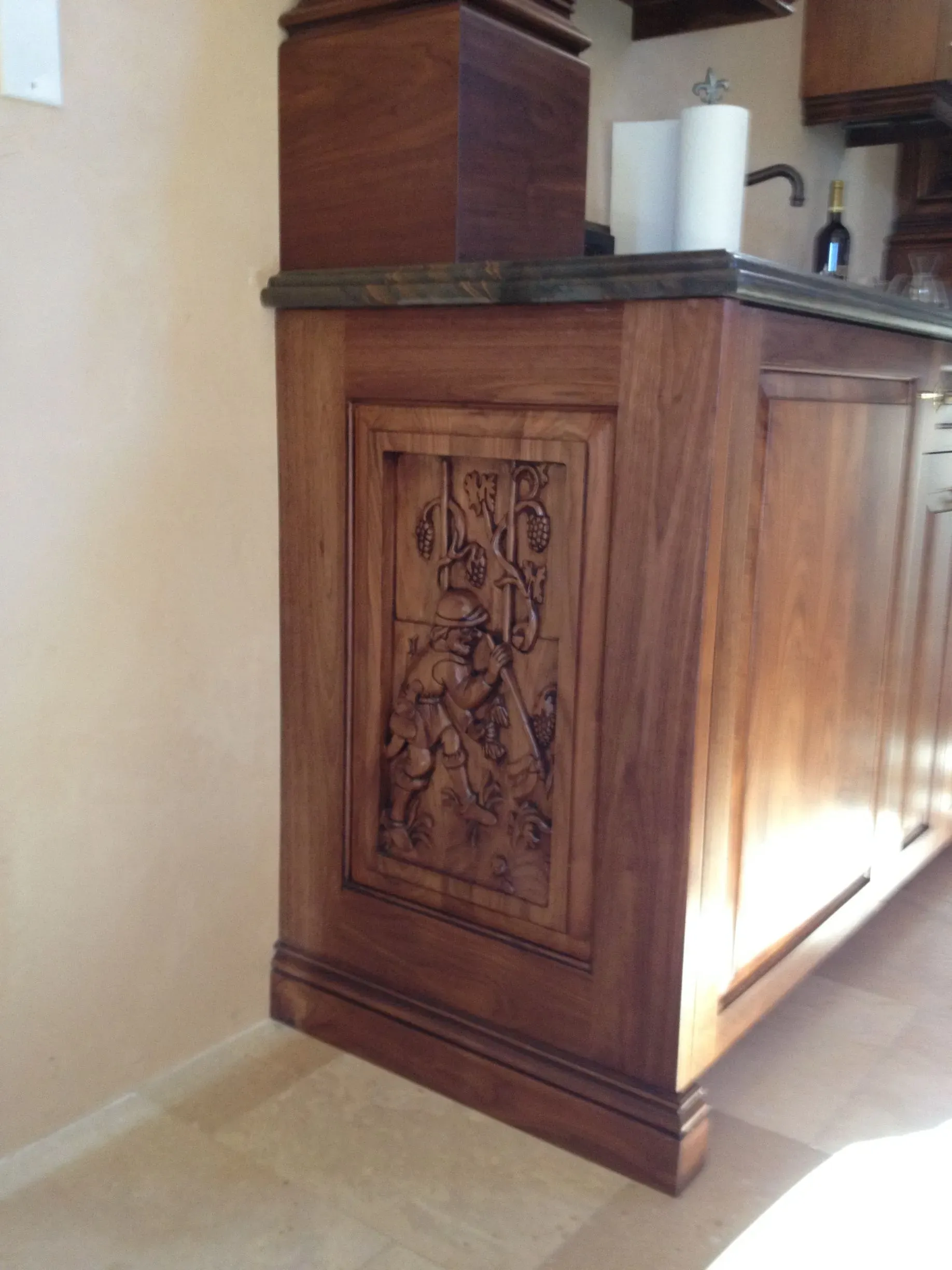 Wooden kitchen cabinet with carved panel, sunlight casting shadows on a tiled floor.