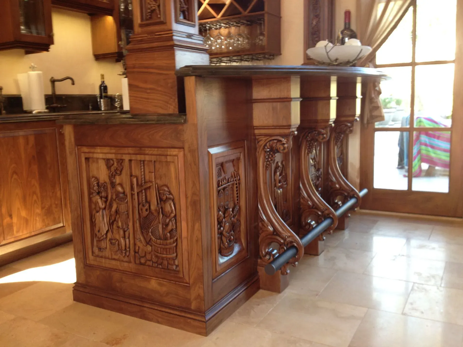 Wooden kitchen island with carved panels and bar stools in a bright, rustic interior
