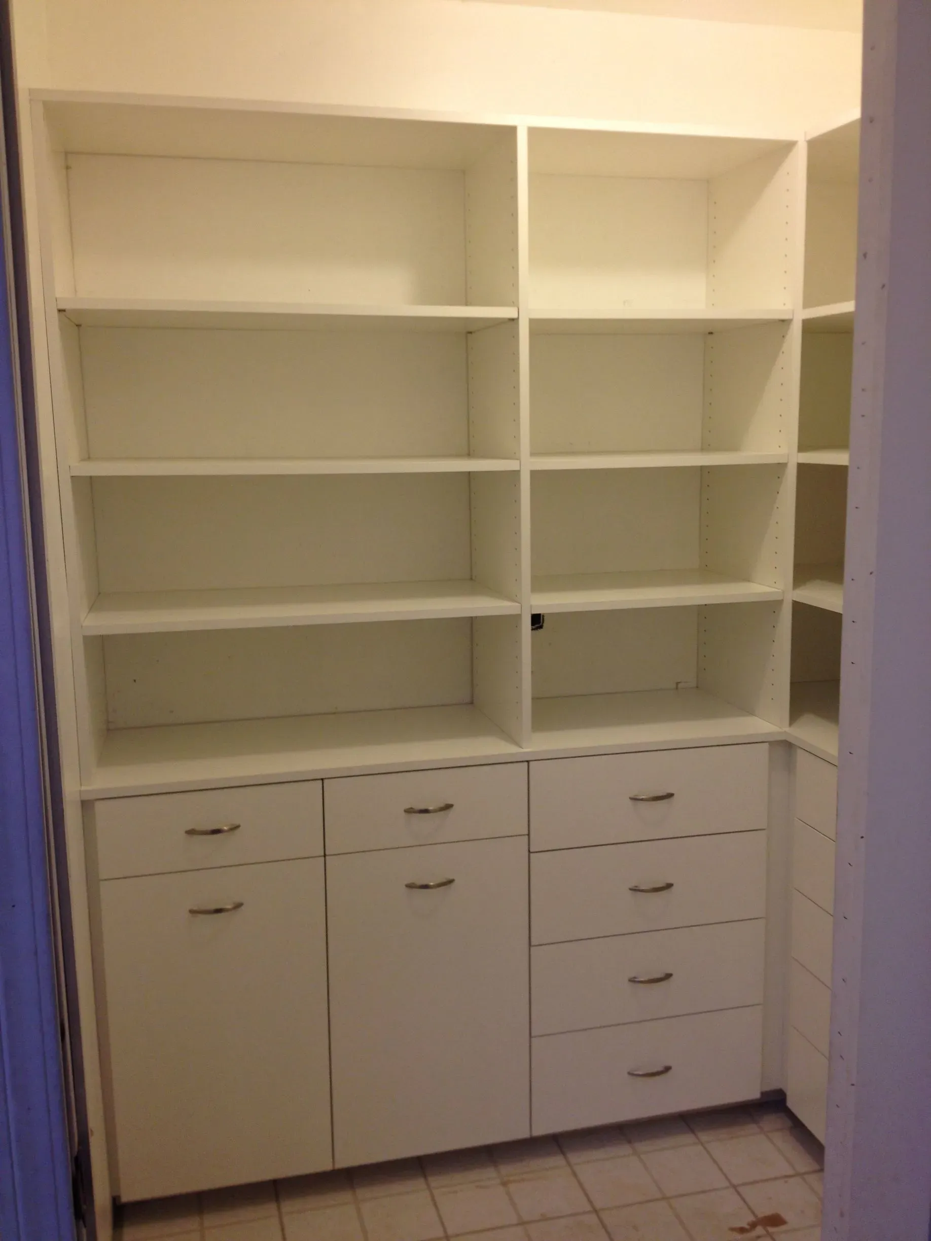 White built-in closet organizer with shelves, drawers, and cabinet doors in a small room.