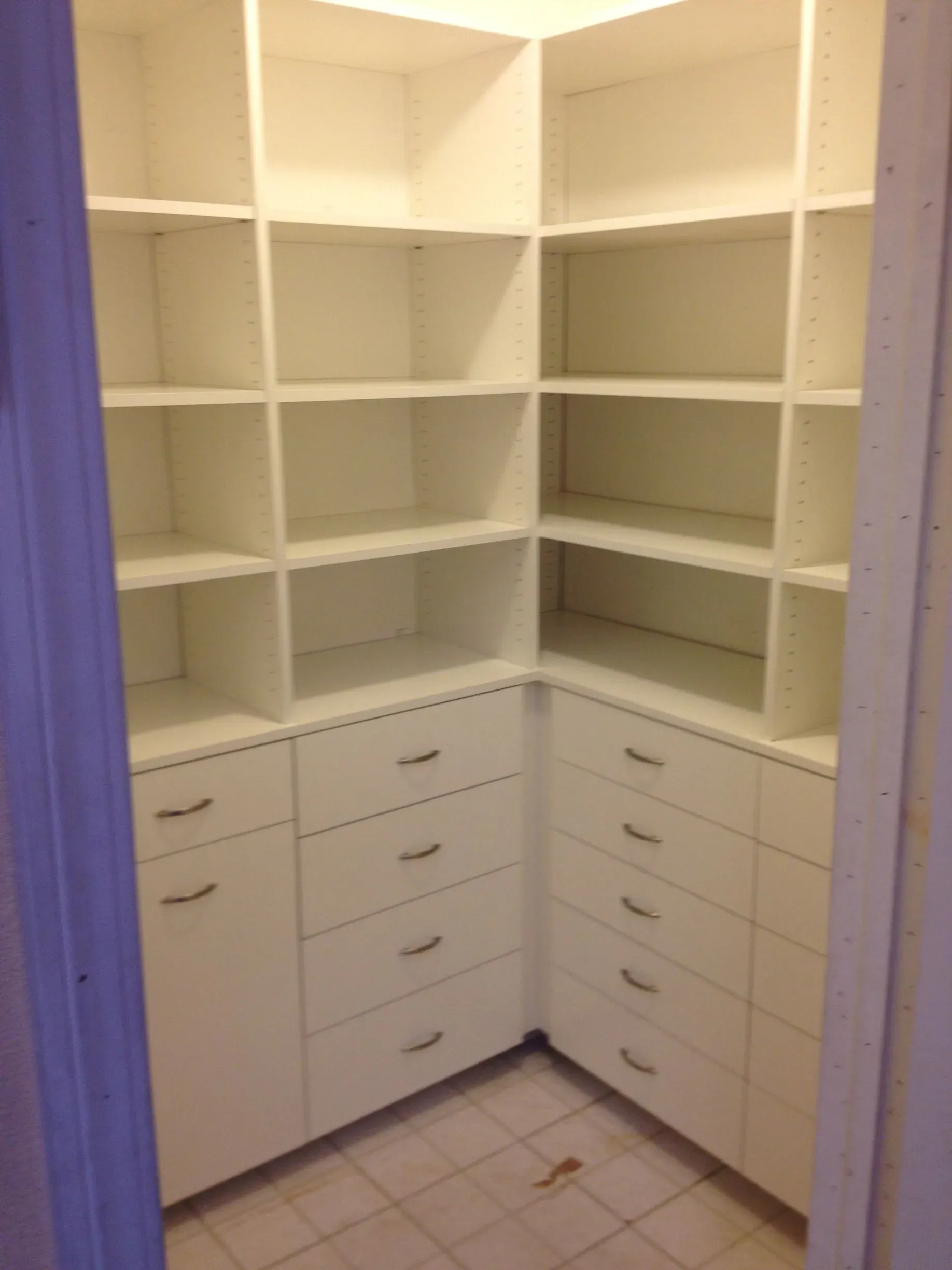 White built-in corner closet with shelves and drawers, empty and well lit.