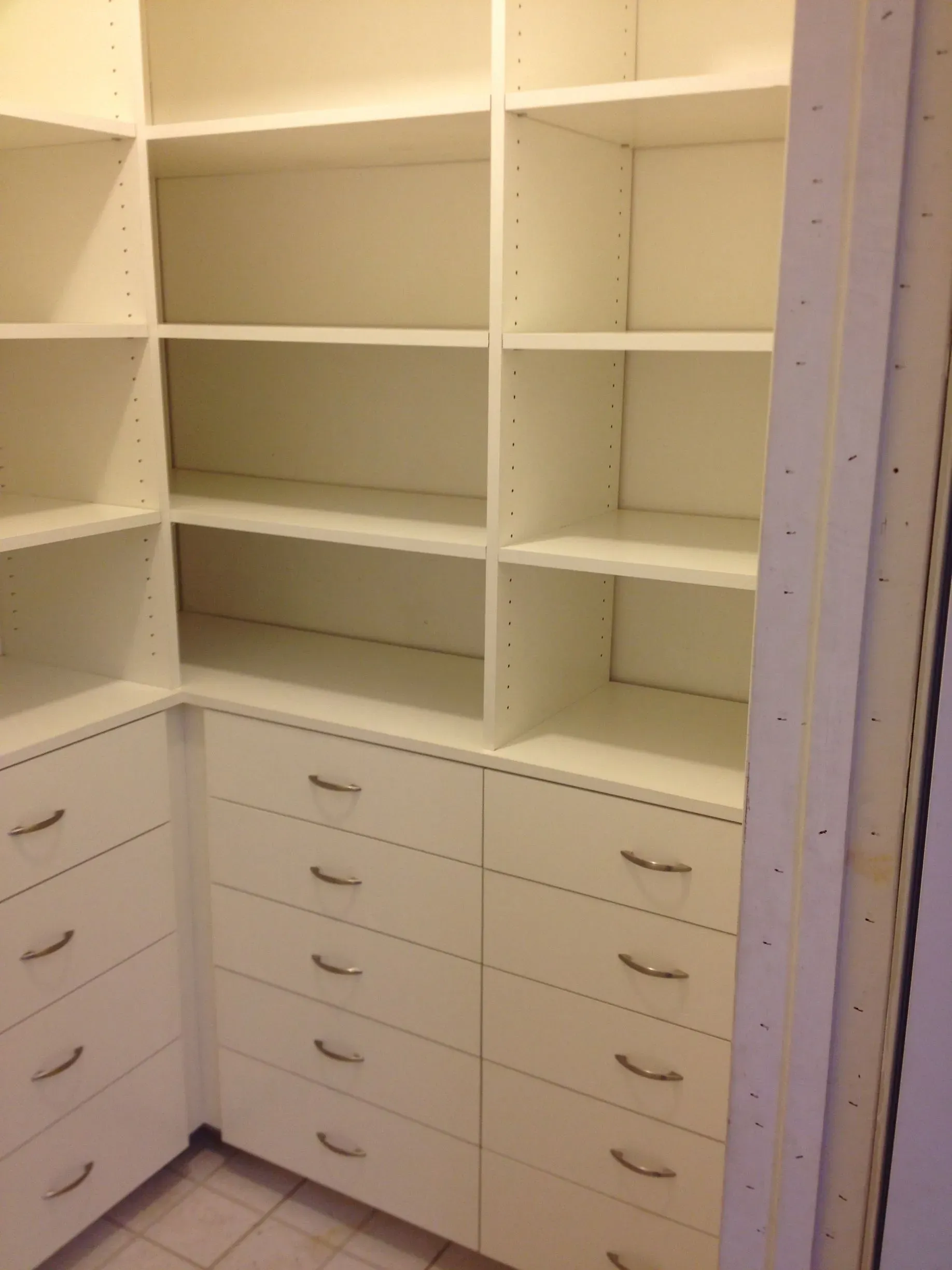 White walk-in closet with built-in shelves and drawers, softly lit and empty