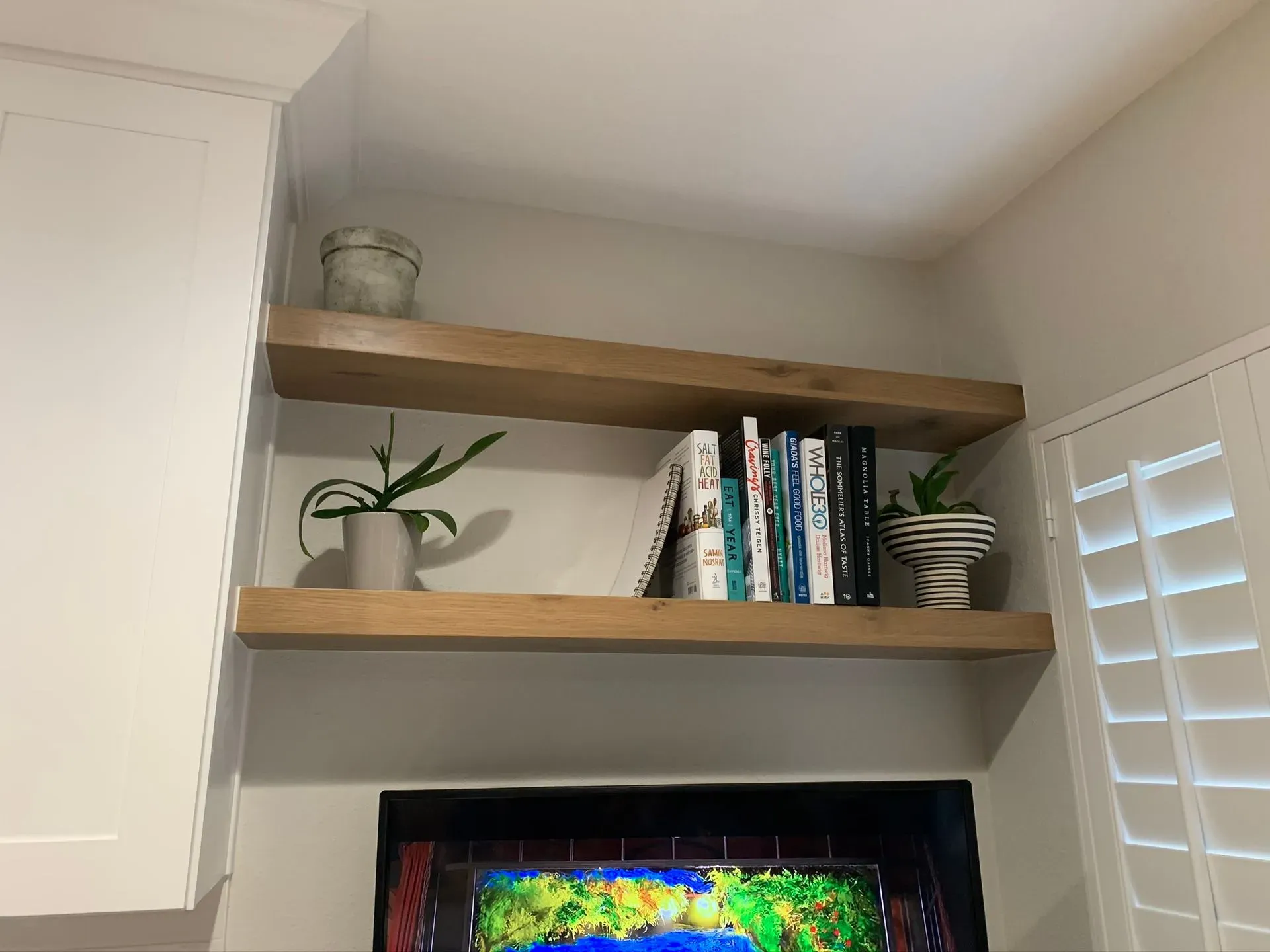 Home office shelves with books, plants, and a TV beneath two wooden floating shelves.