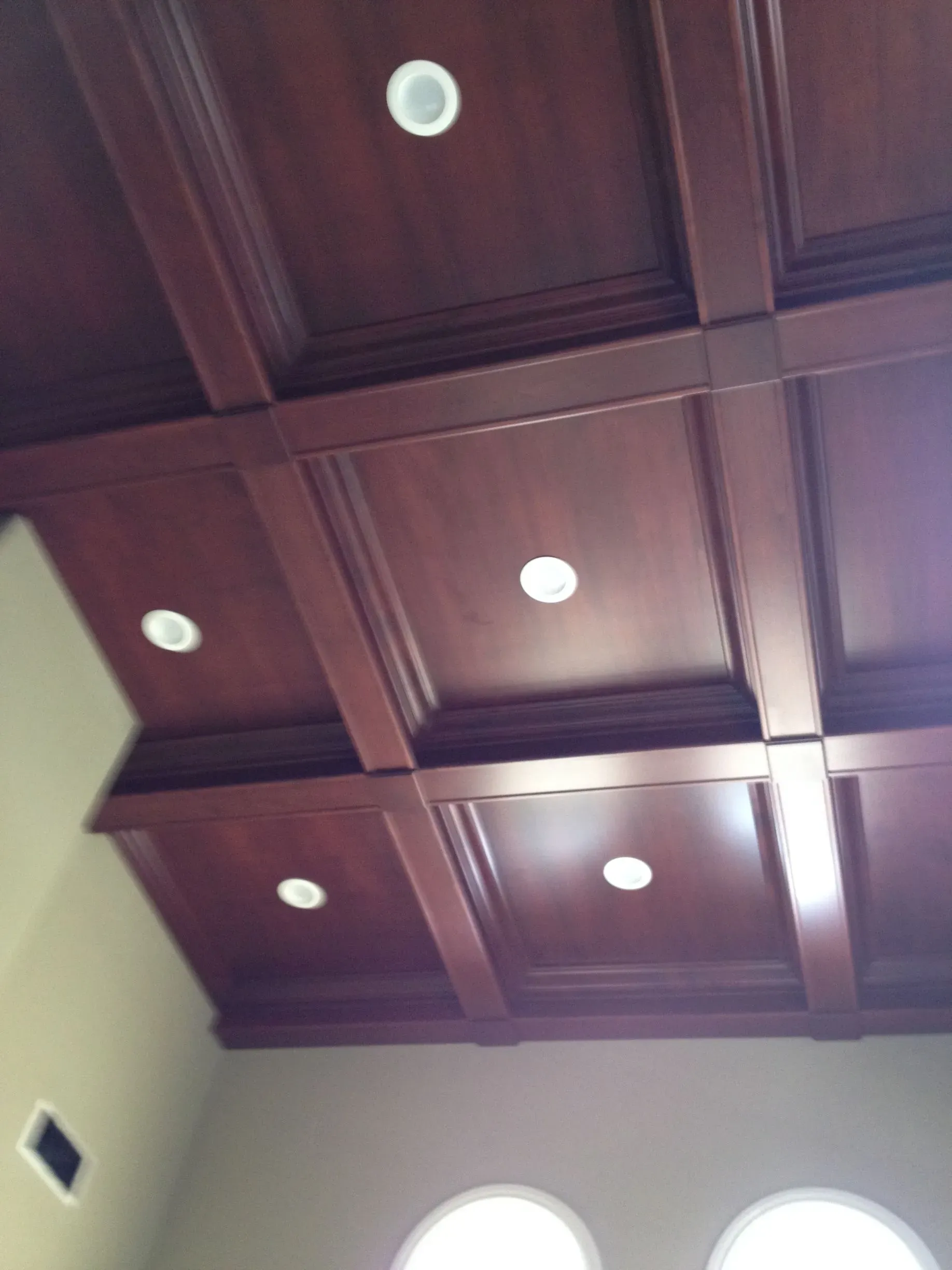 Dark wooden coffered ceiling with recessed lights and a round window at the bottom edge