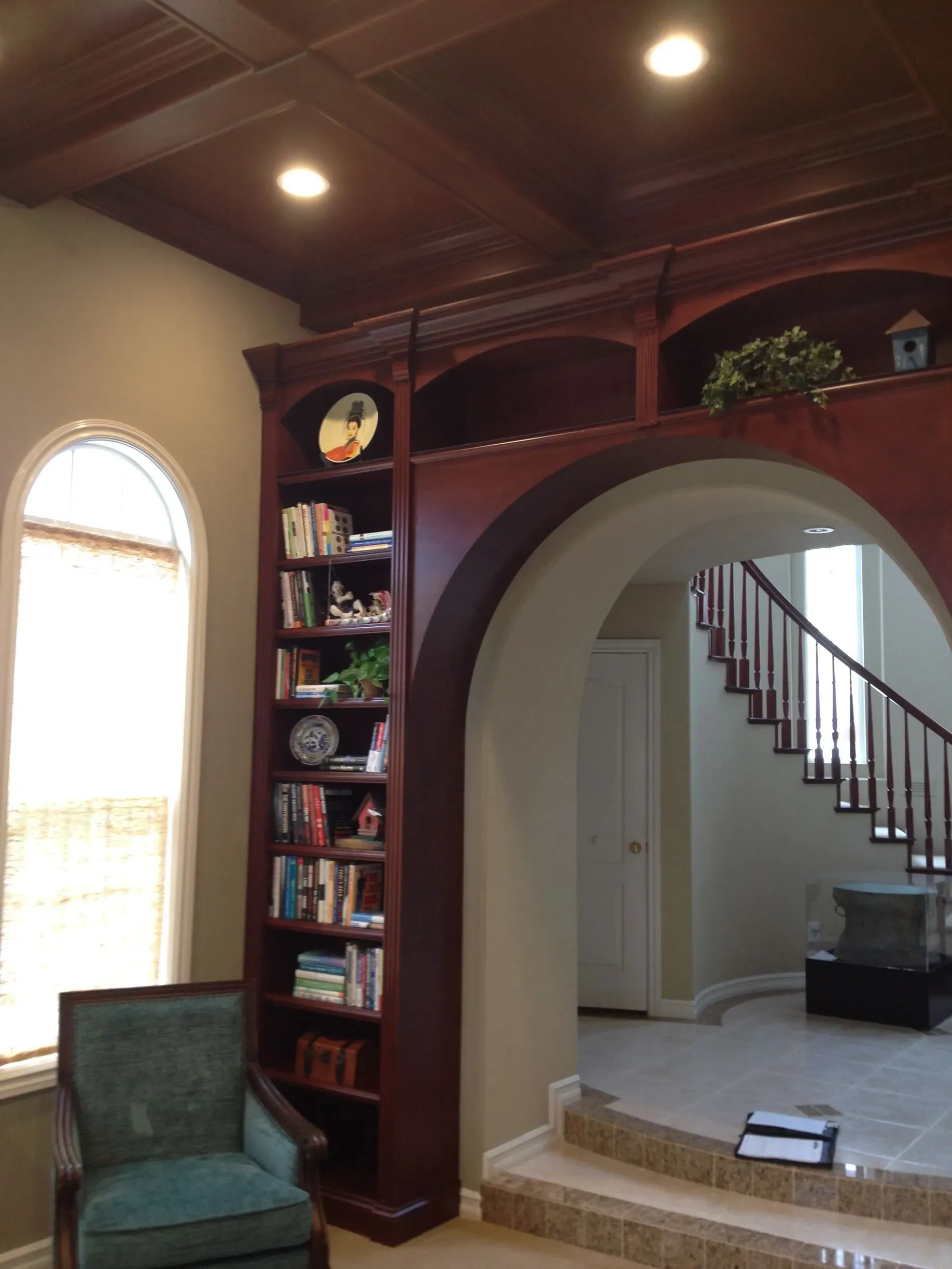 Living room with arched entry, built-in bookshelf, teal chair, and staircase in the background