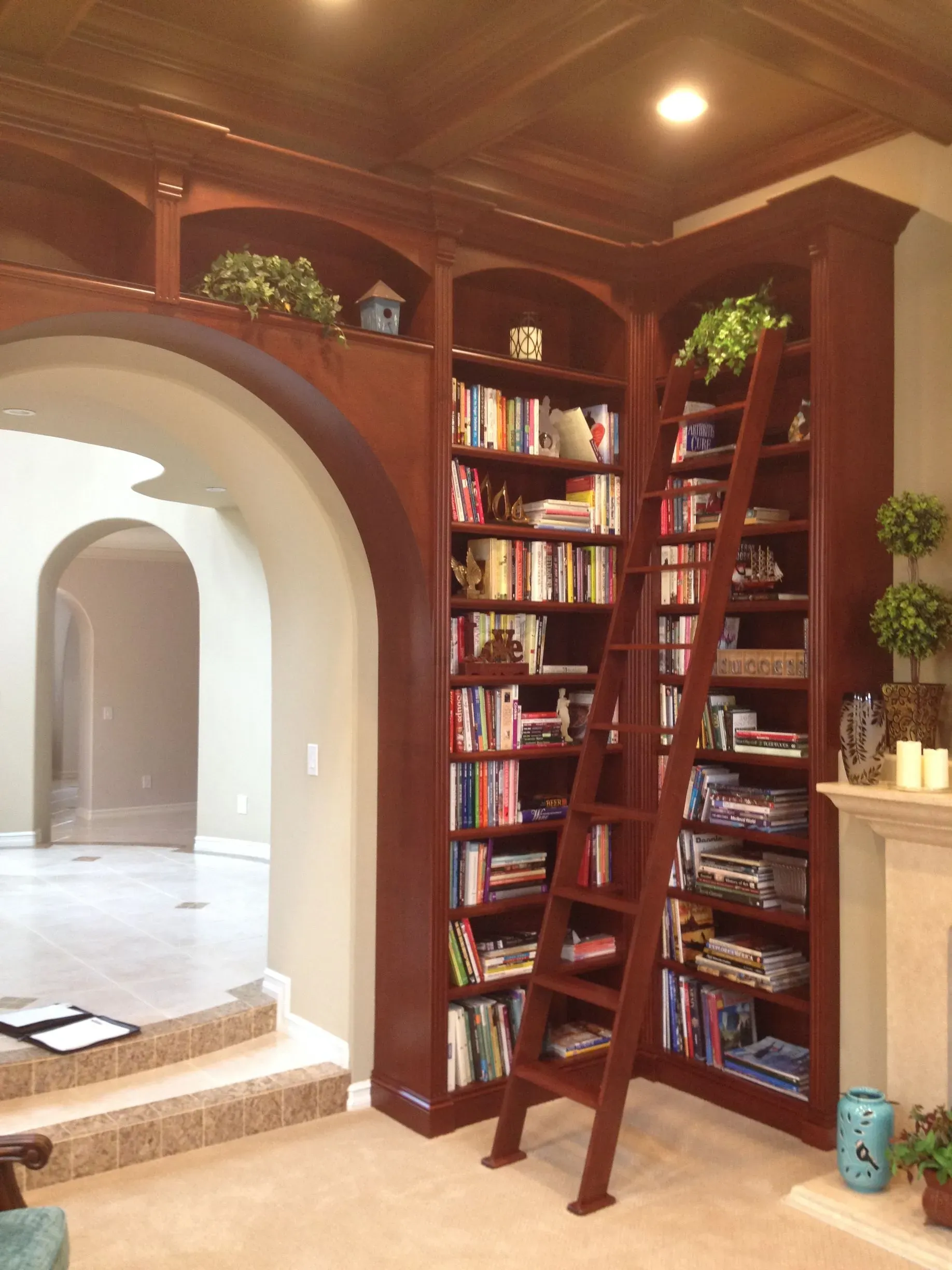 Wooden ladder on built-in bookshelf in a warmly lit arched hallway with books and plants