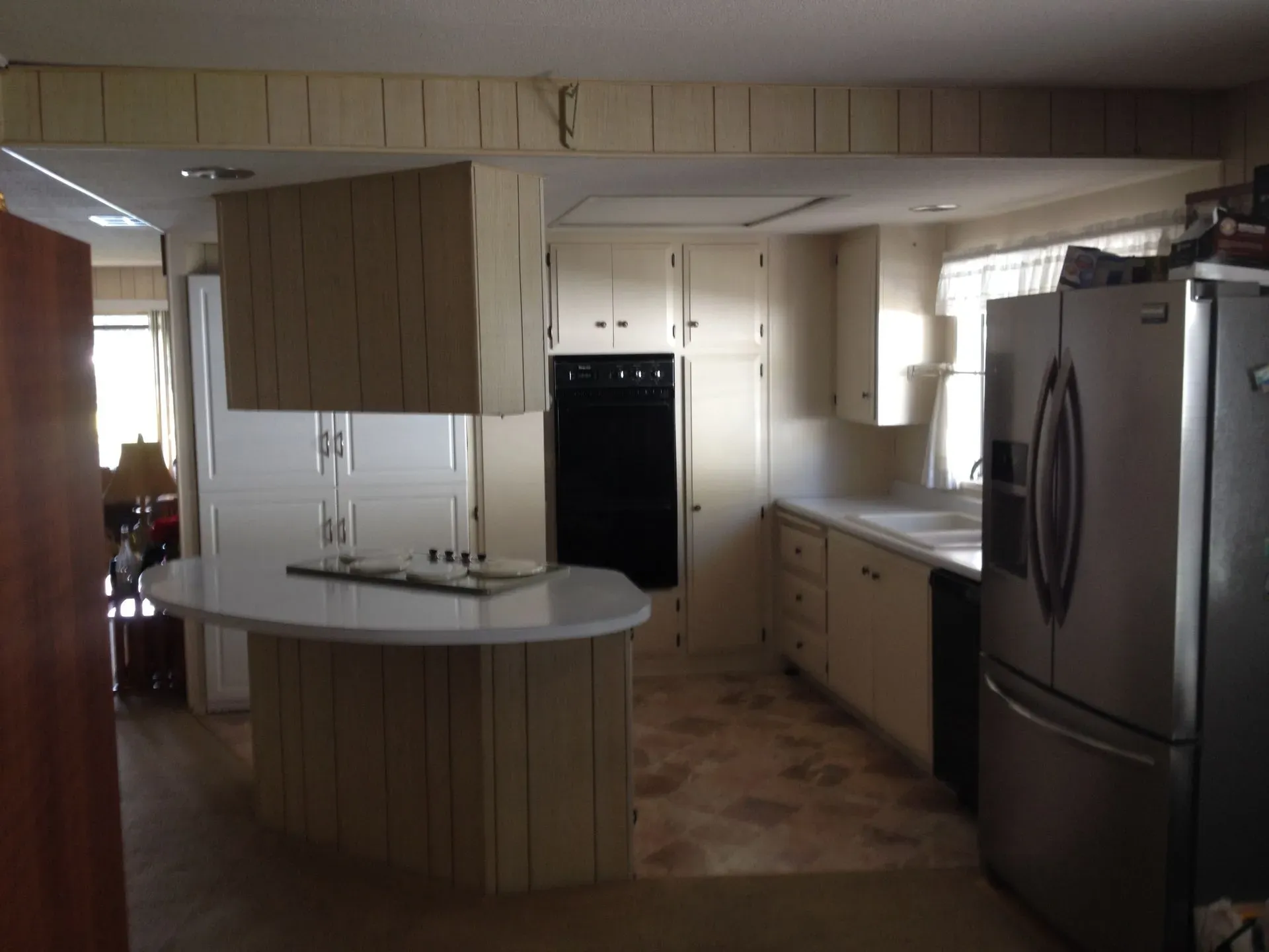 Modern kitchen with light wood cabinets, curved island, and stainless steel refrigerator and oven