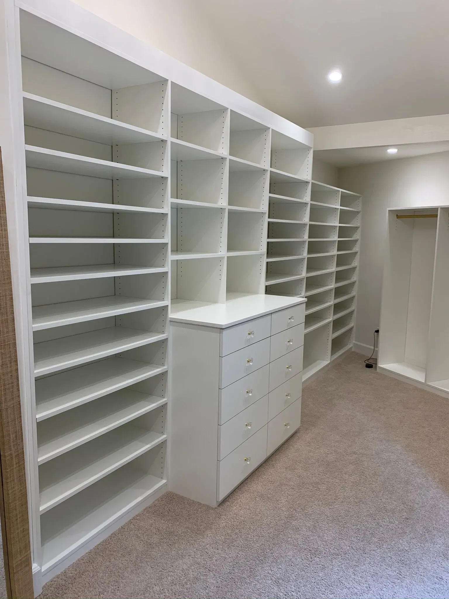 Walk-in closet with white built-in shelves, drawers, and beige carpet under ceiling lights