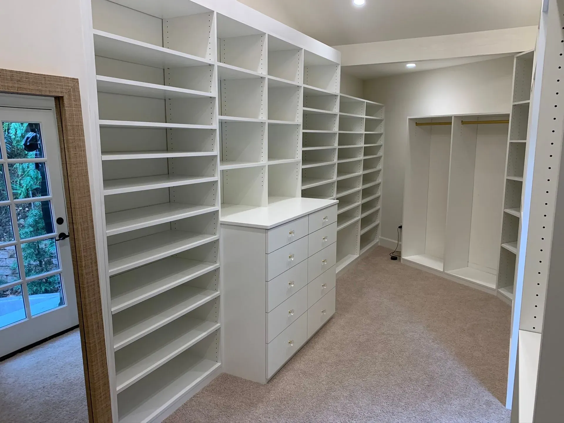 Empty walk-in closet with white shelving, drawers, and a built-in hanging area on beige carpet.