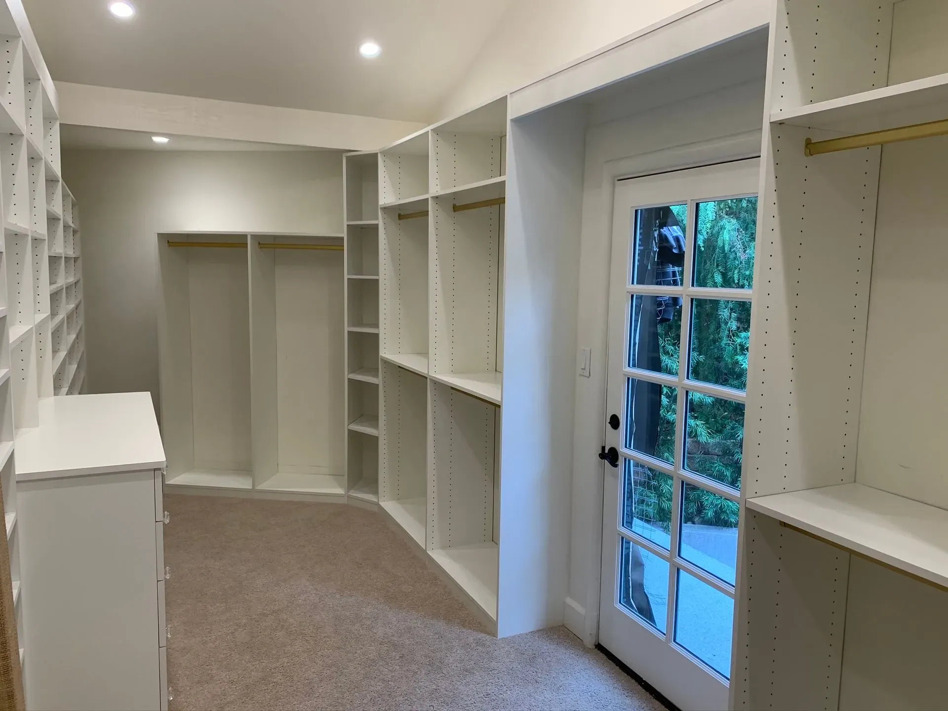 Empty walk-in closet with white shelving, beige carpet, and a glass door to outside.