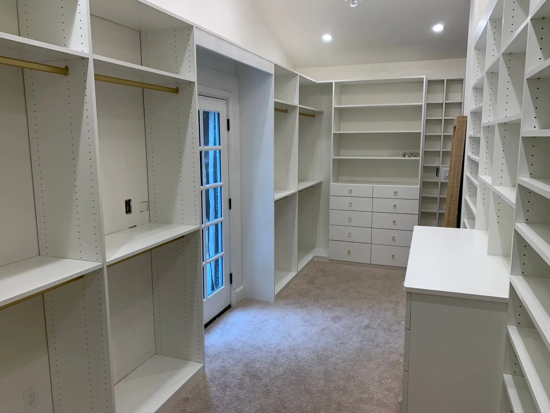 Empty white walk-in closet with built-in shelves, drawers, and a window.