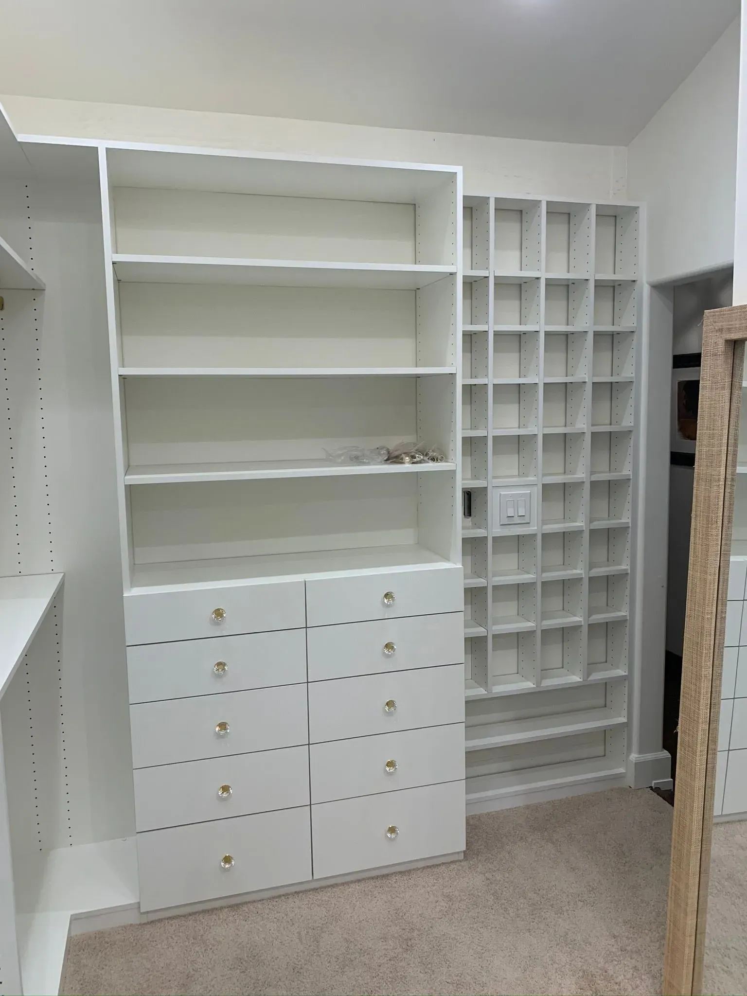 White closet with empty shelves, many small drawers, and a tall cubby organizer in a storage room.