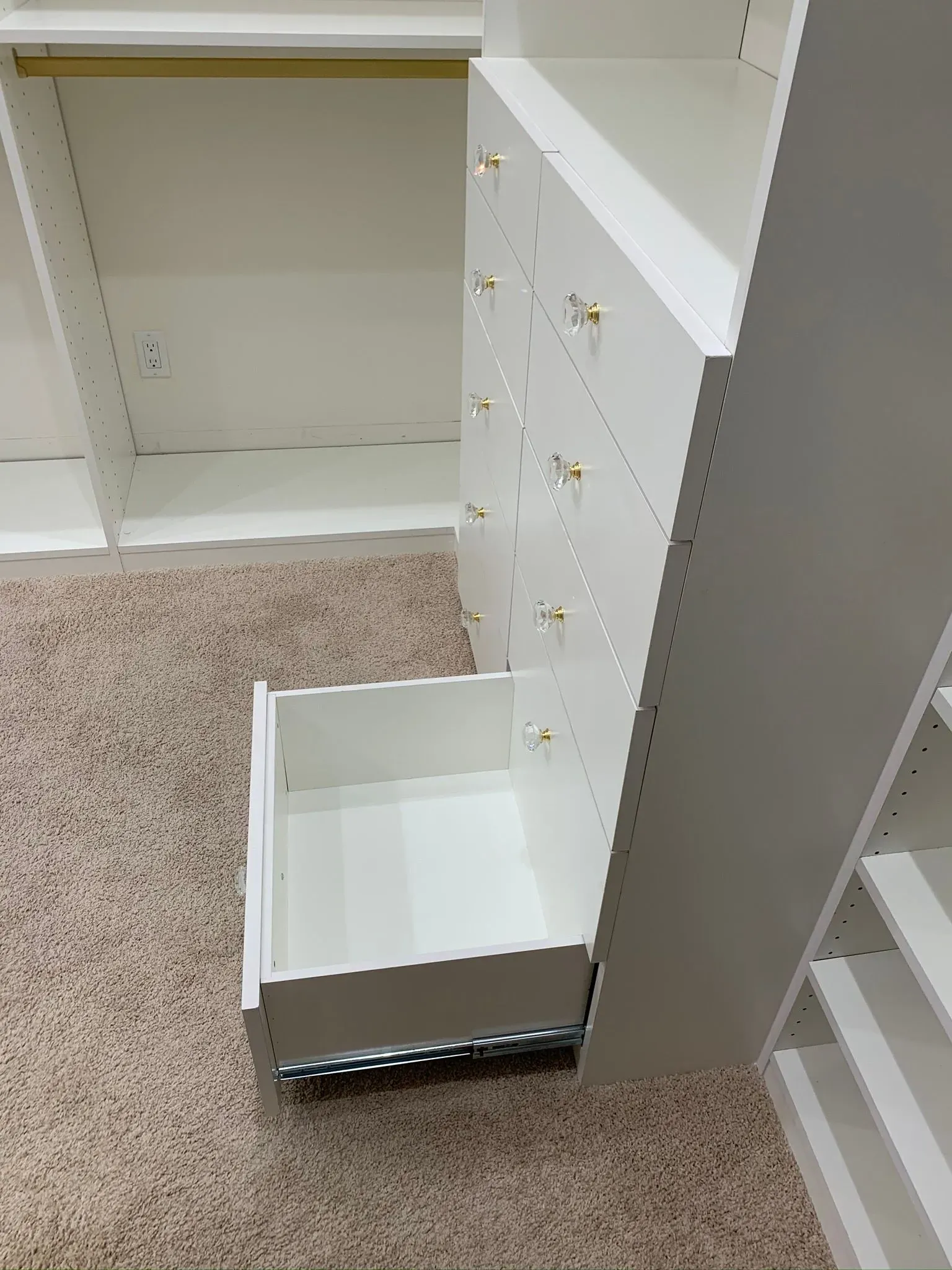 Open white dresser drawer pulled out over beige carpet, with empty shelves beside it.