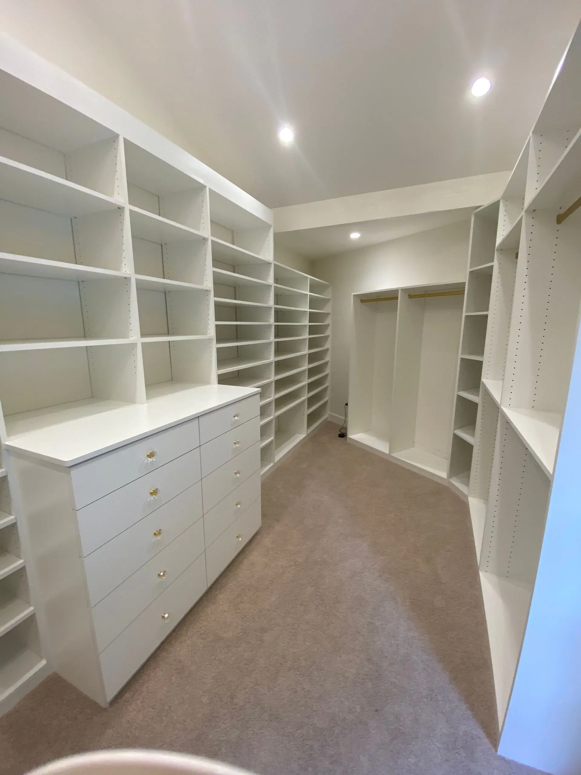 Bright walk-in closet with white shelves, drawers, and carpeted floor.