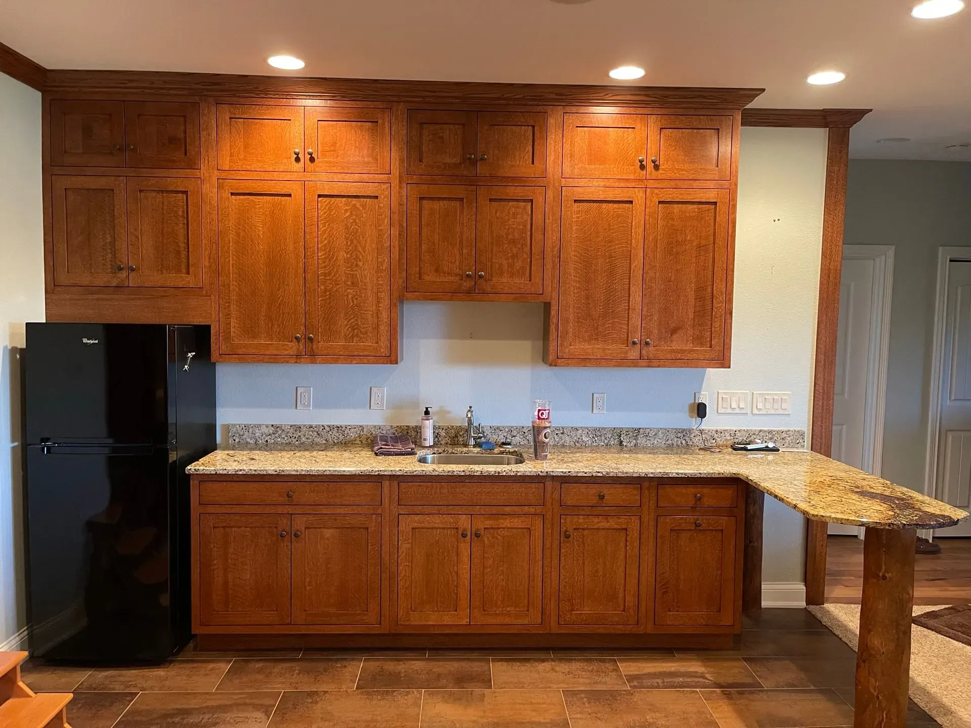 Wooden kitchen with black refrigerator, granite counters, and a small breakfast bar