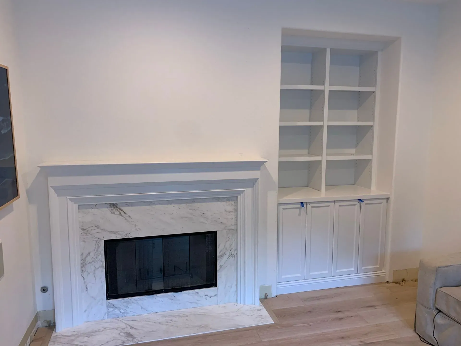 White living room wall with a marble fireplace and built-in shelves/cabinets, partial sofa at right
